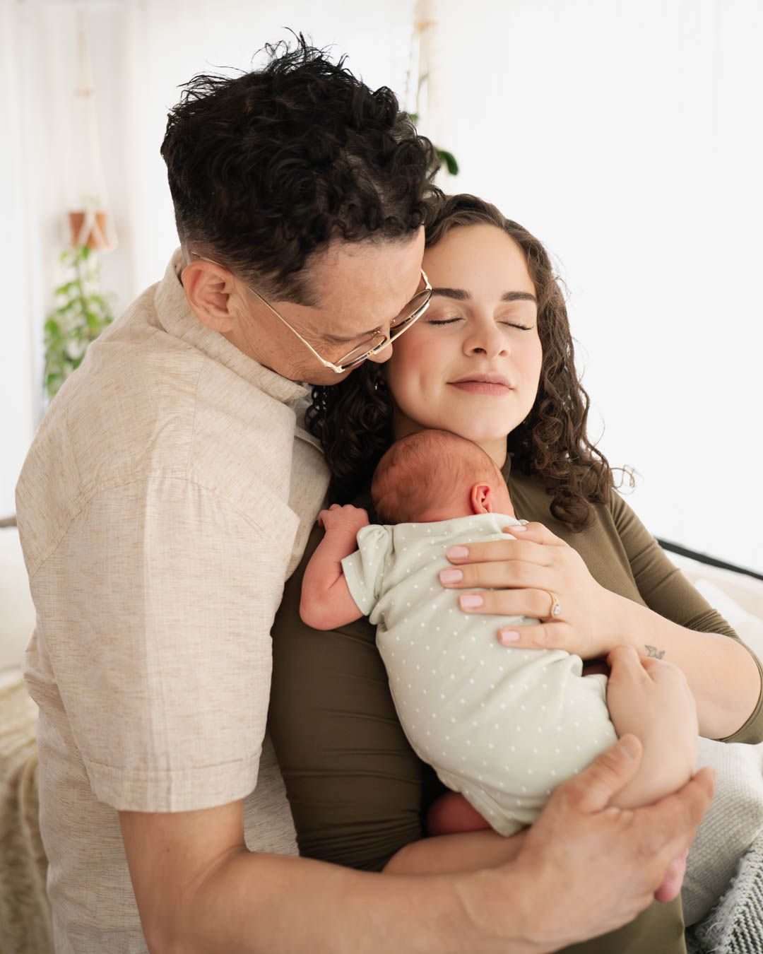 Mother holding baby with father hugging from behind them