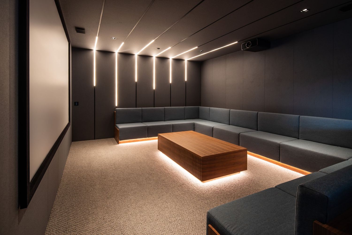 Minimalist lounge room with illuminated ceiling lights and blue sectional seating around a wooden coffee table.