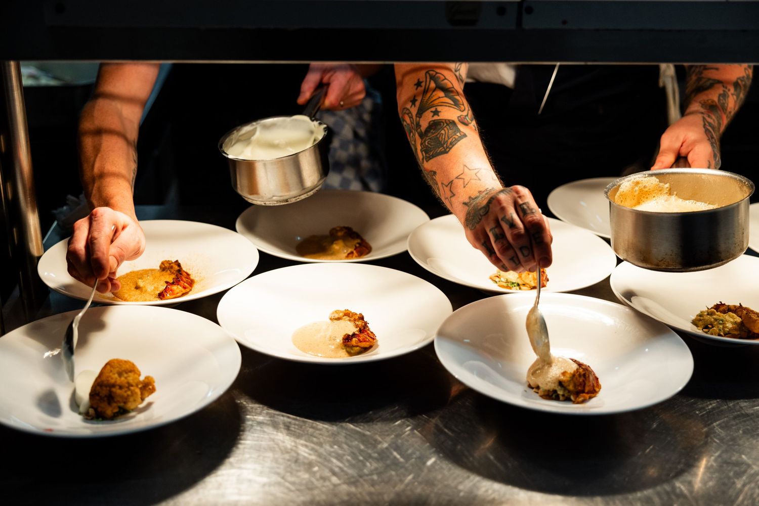 Multiple chefs working in synchronization to plate dishes in a restaurant kitchen.