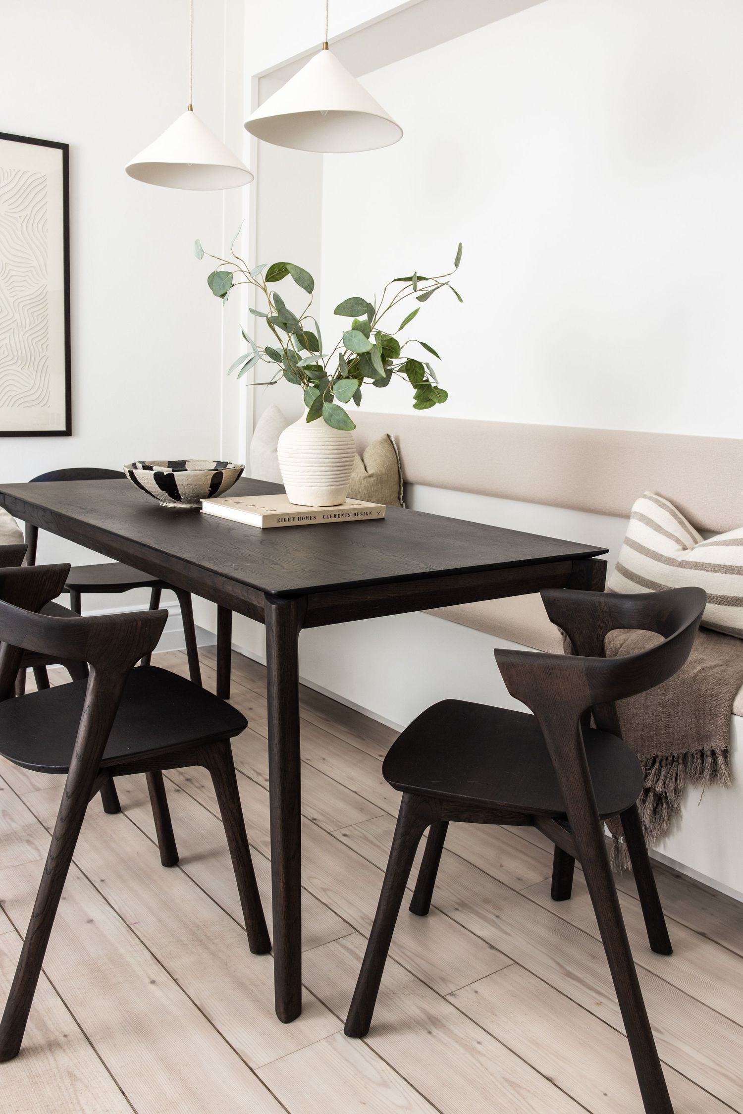 Scandinavian dining area featuring black chairs and dark wood table against white walls.