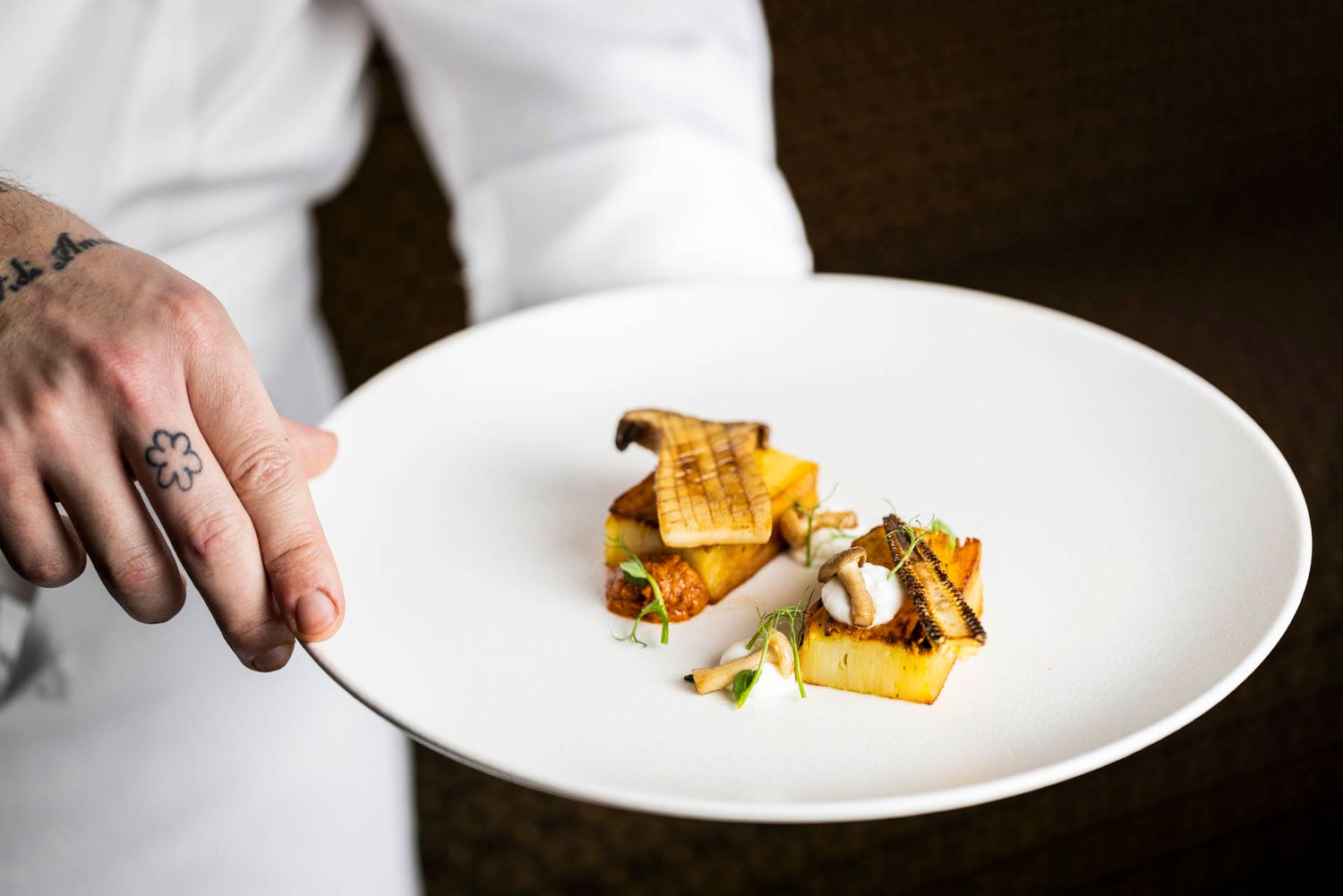 Chef plating an elegant dish with golden components on a white plate.