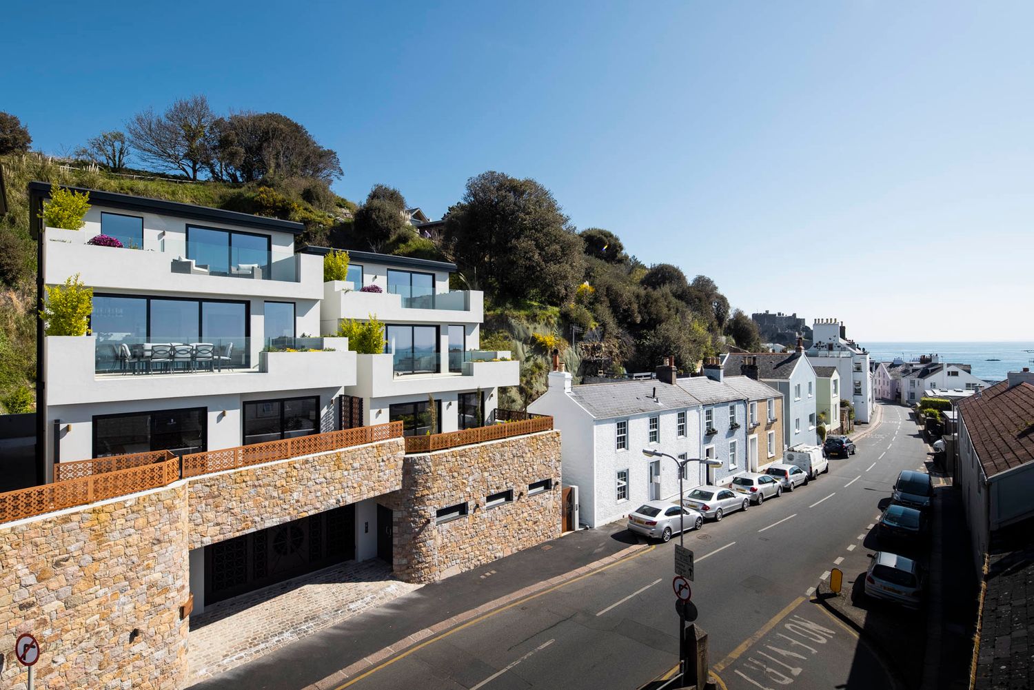 Modern luxury homes and buildings along a coastal street with ocean views.