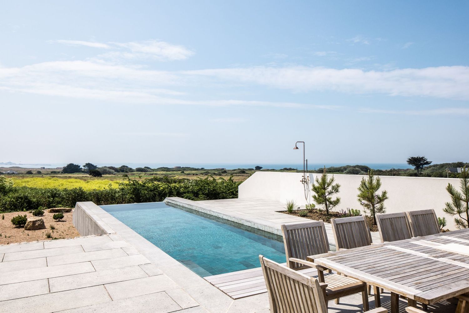 Luxury outdoor patio area with lounge chairs and infinity pool overlooking scenic coastal landscape.