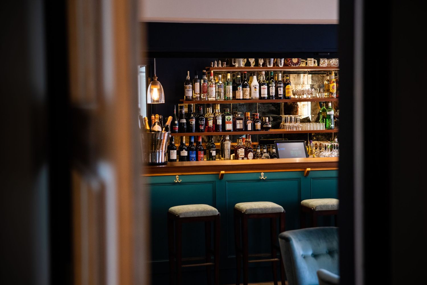 Dimly lit bar interior with bottles illuminated on shelves and bar stools in the foreground.