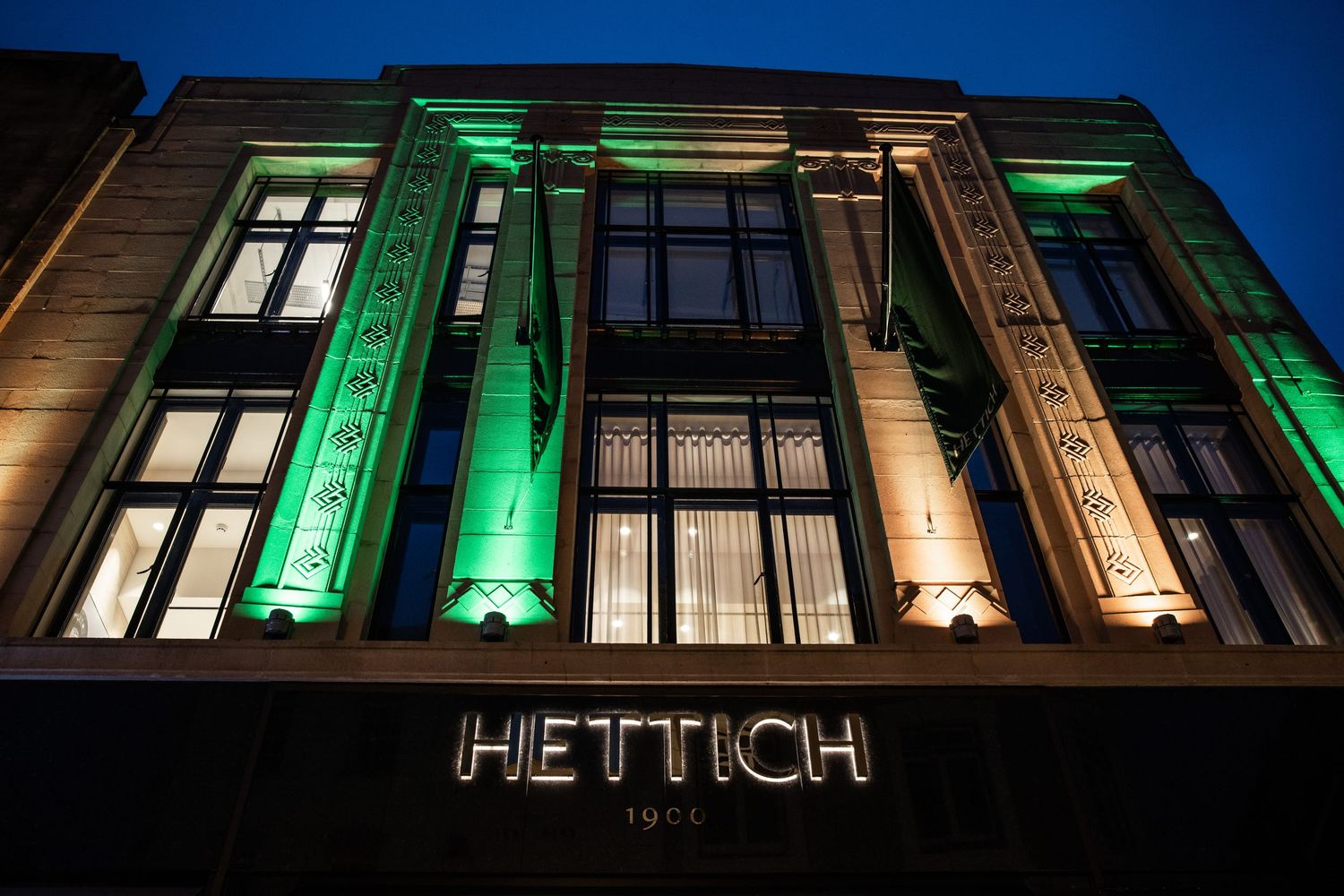 Illuminated Hettich building exterior with green and amber lighting at night.