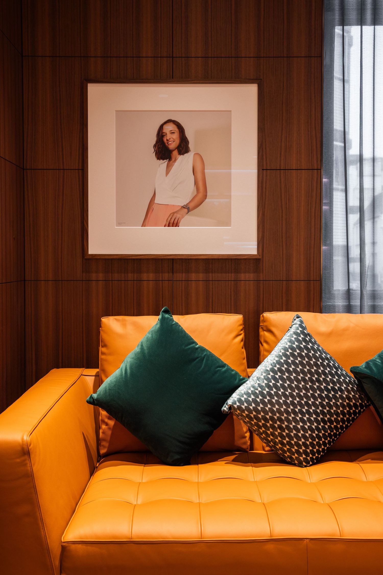 Contemporary lounge area with orange leather sofa and green accent pillows against wood paneling.
