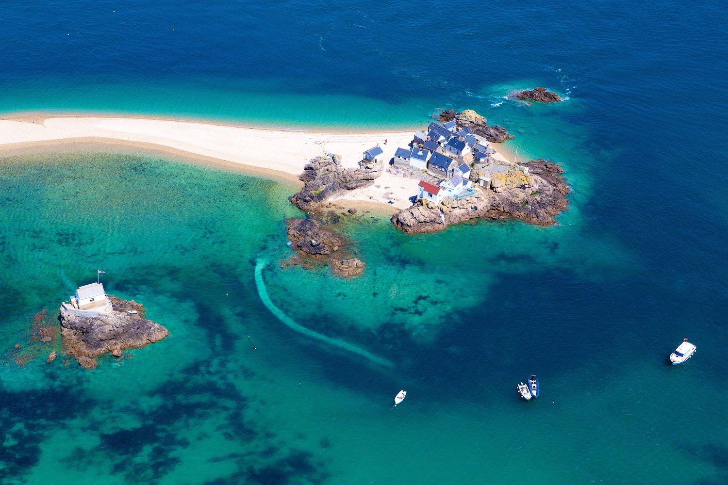 Aerial view of turquoise waters surrounding small rocky islands with boats anchored nearby.