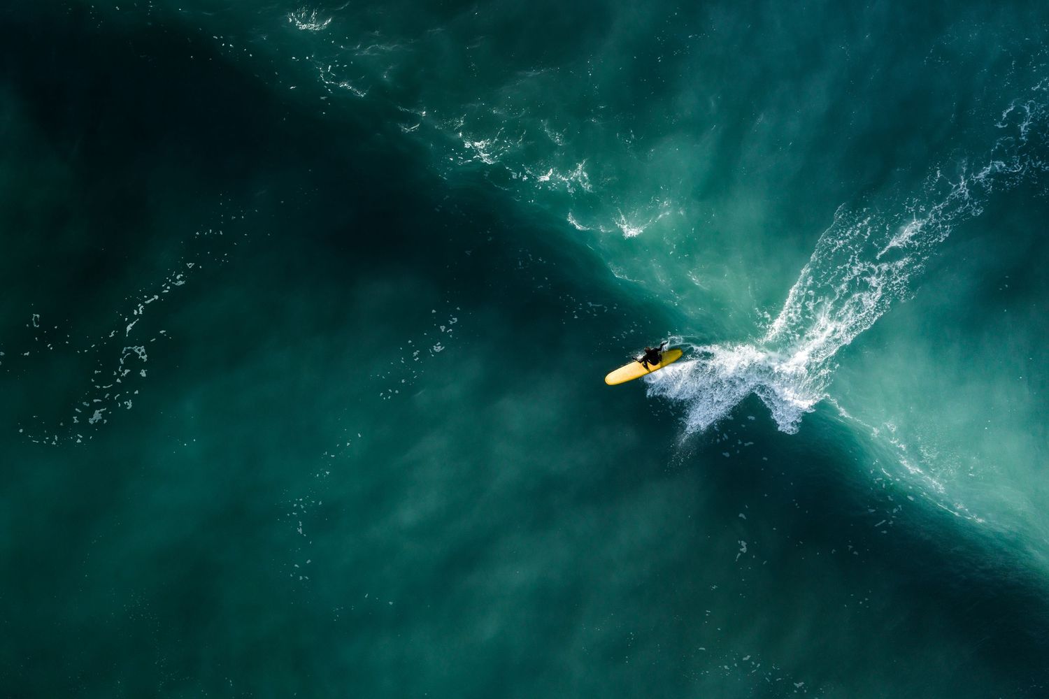 Aerial shot of surfer riding a perfect turquoise wave in deep ocean waters.