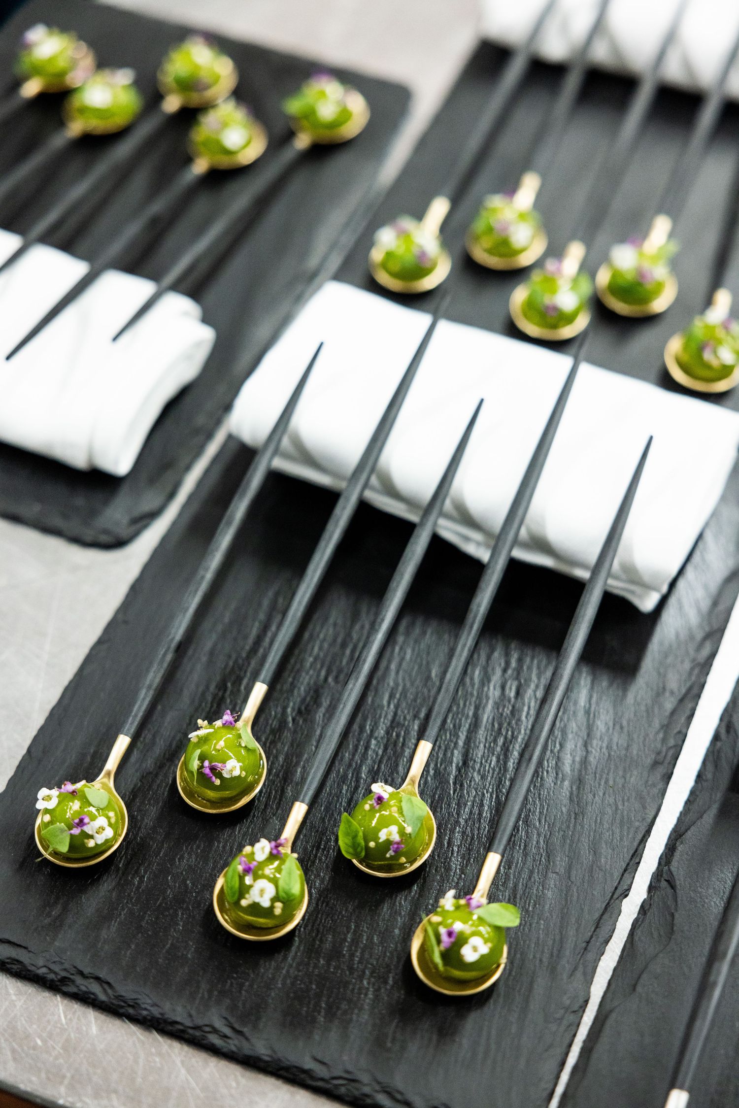 Elegant appetizers arranged on black slate spoons with microgreens and garnishes.