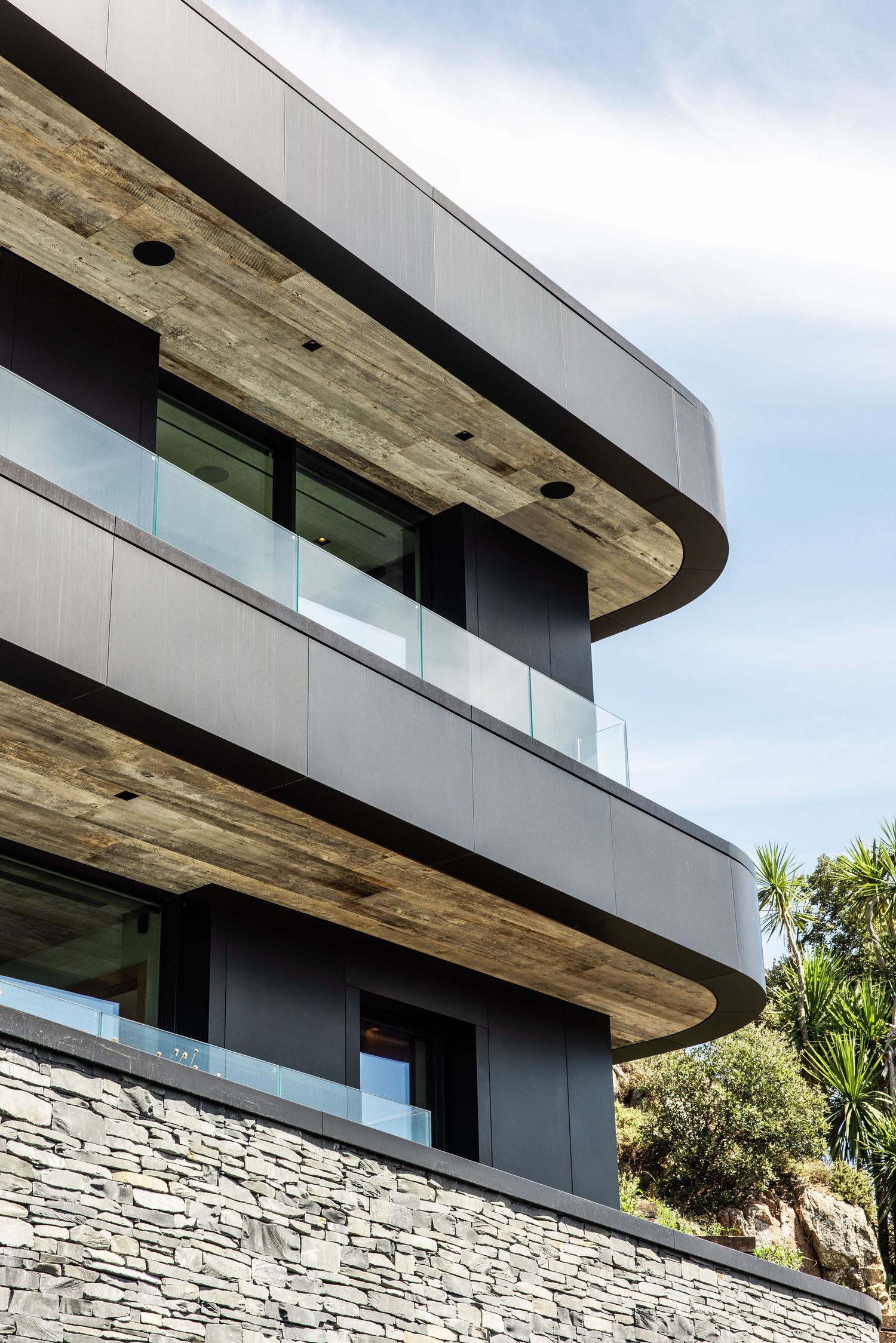 Contemporary architecture featuring curved wooden overhangs and stone facade with glass railings.