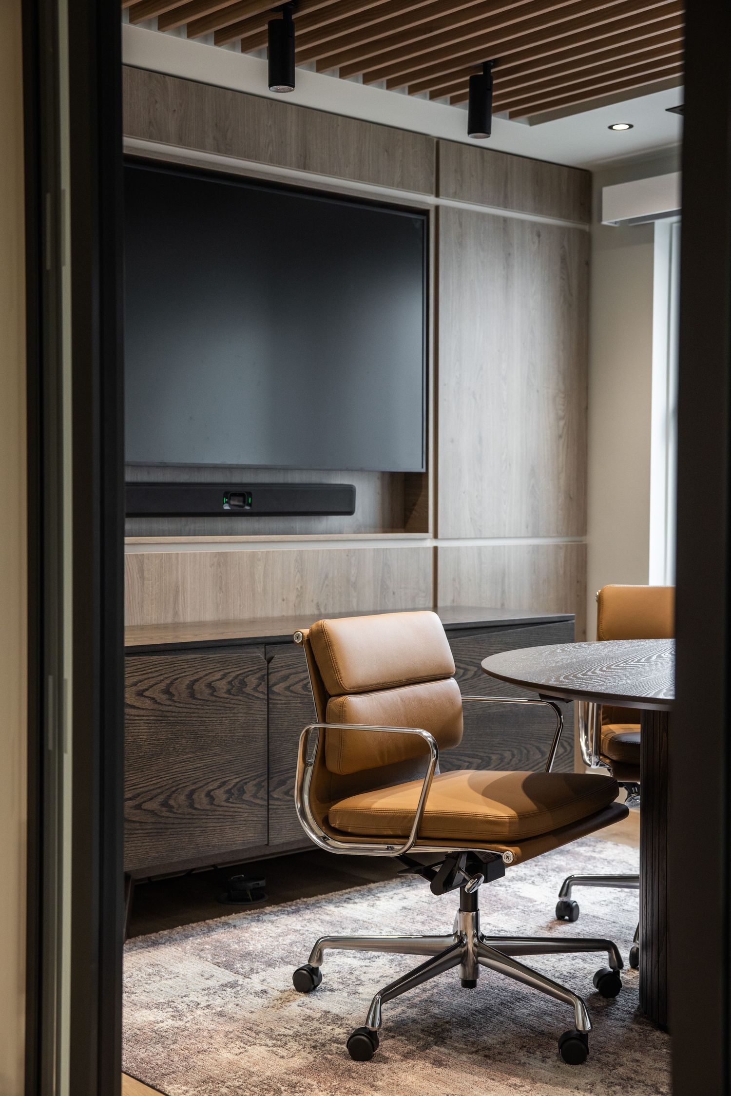 Elegant meeting room with tan leather chairs and wooden wall panels featuring built-in display screens.