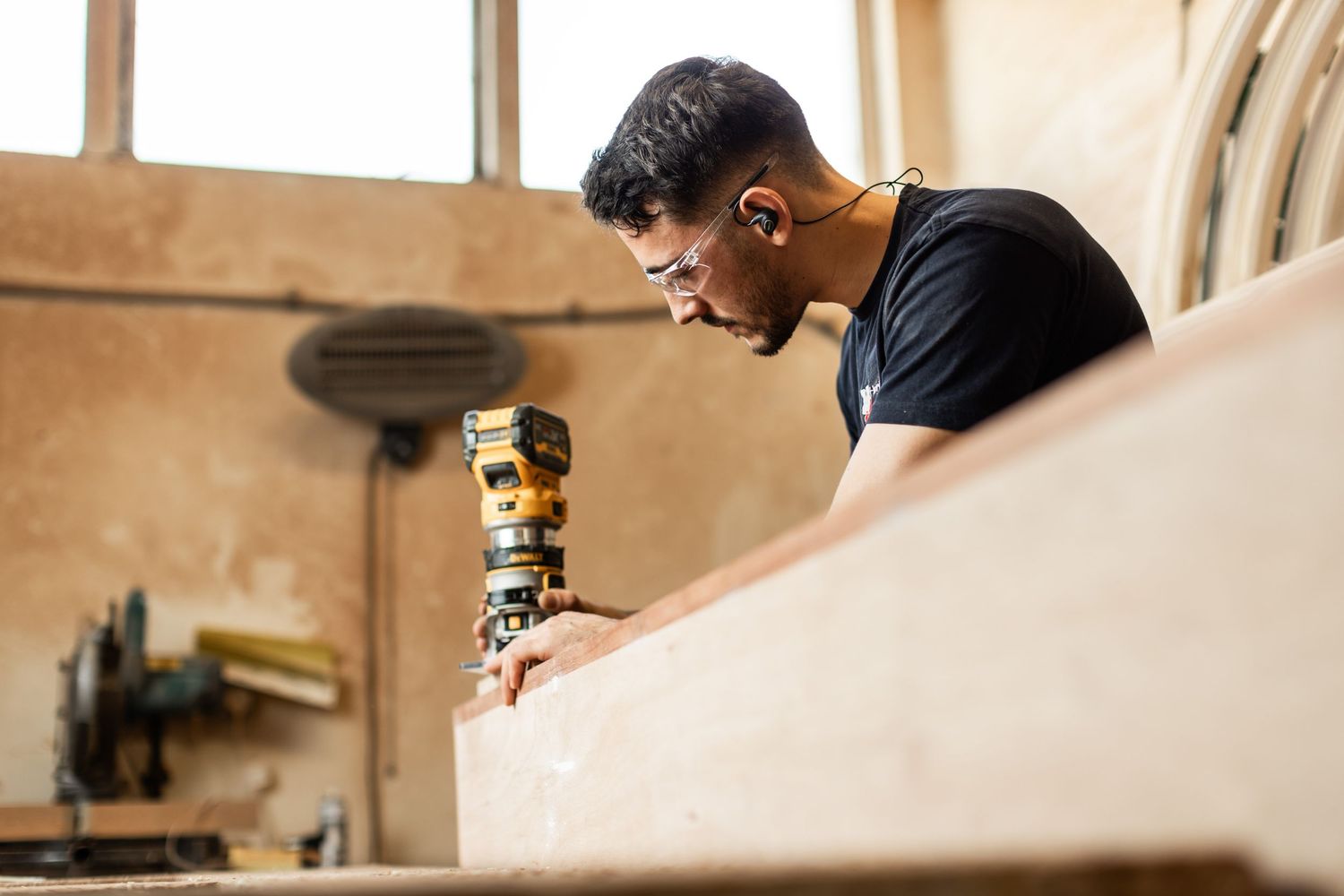 Craftsmen working with power tools and wood materials in a carpentry workshop.