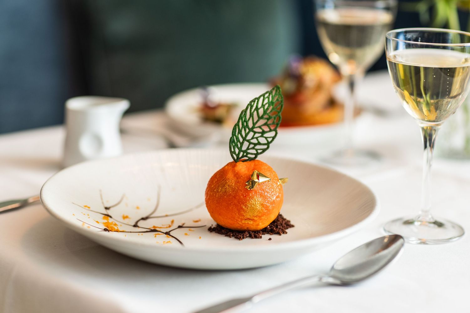 Elegant plated dessert with citrus garnish and wine glass in upscale restaurant setting.