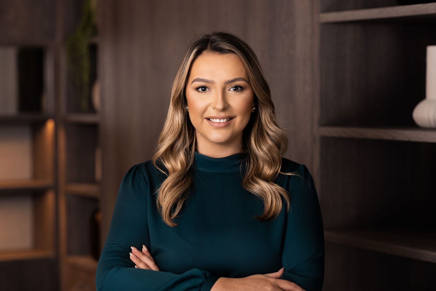 Professional in a dark teal turtleneck sweater poses with crossed arms against a dark background.
