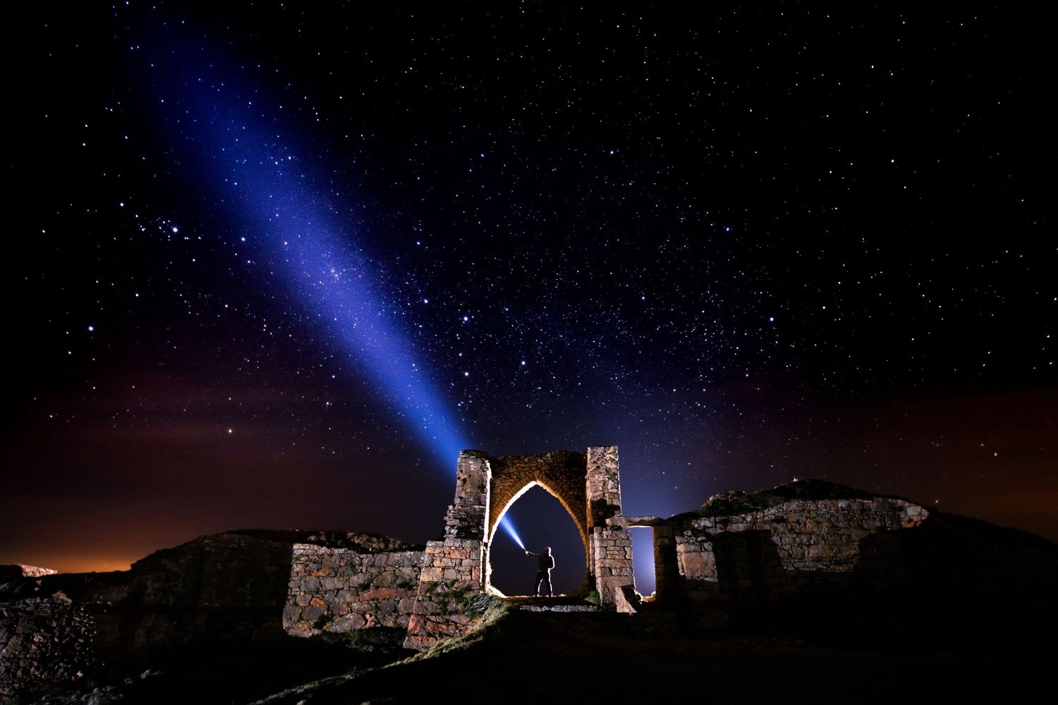 Blue spotlight beam illuminating ancient stone ruins against a starry night sky.