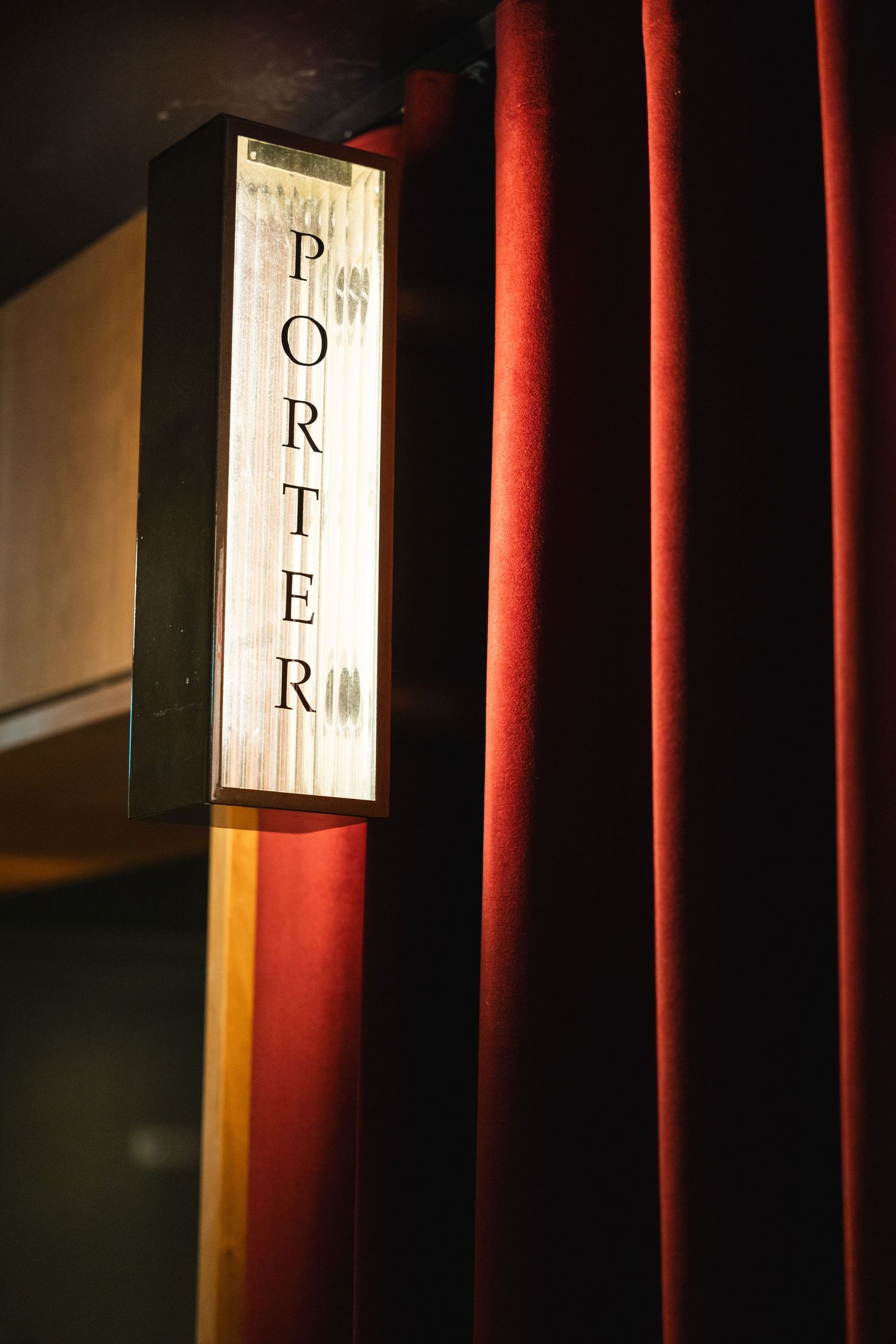 Illuminated Porter sign mounted on wall with red velvet curtain.