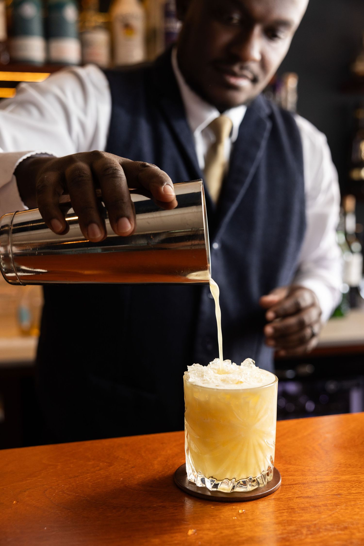 Bartender pouring a creamy cocktail into a glass at an upscale bar.