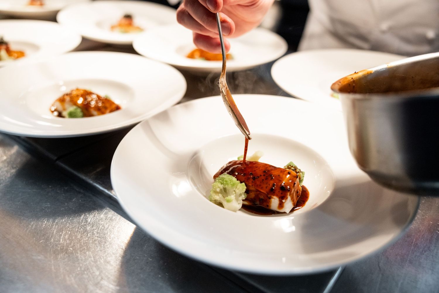 Fine dining plates being garnished with sauces and final touches.