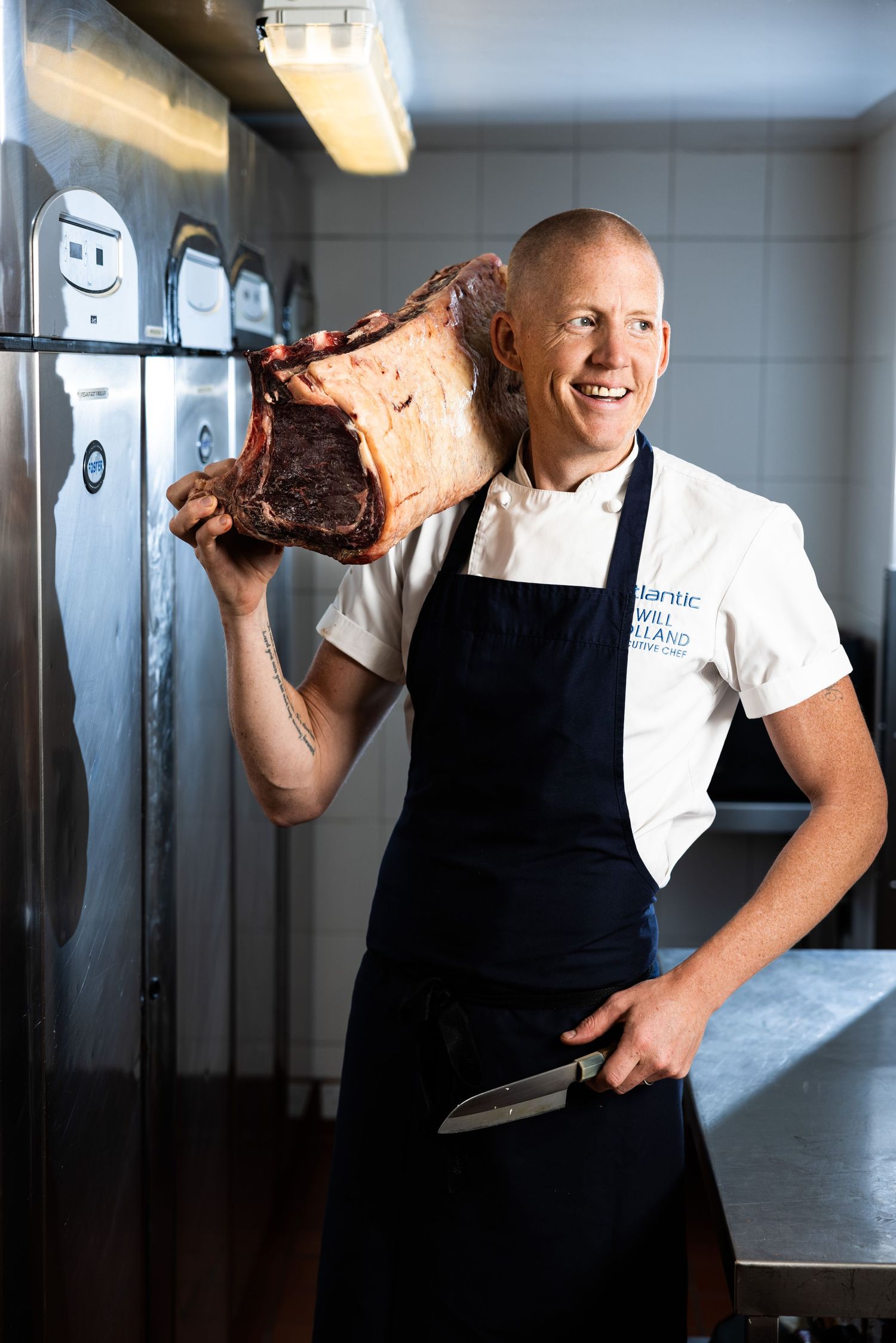 Chef displaying large cuts of meat in a professional kitchen environment.