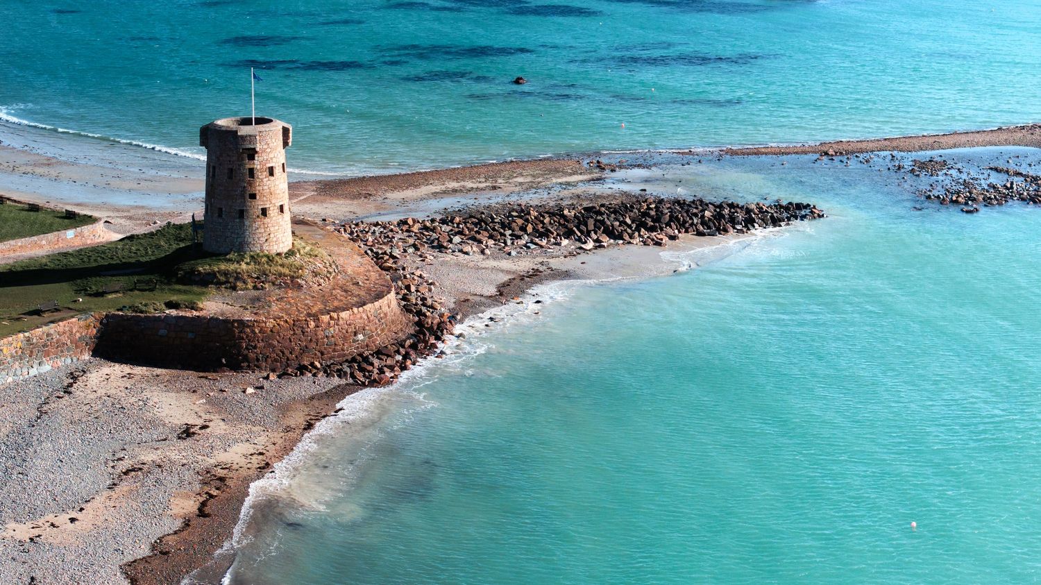 Panoramic view of a coastal watchtower overlooking turquoise waters and rocky shoreline.