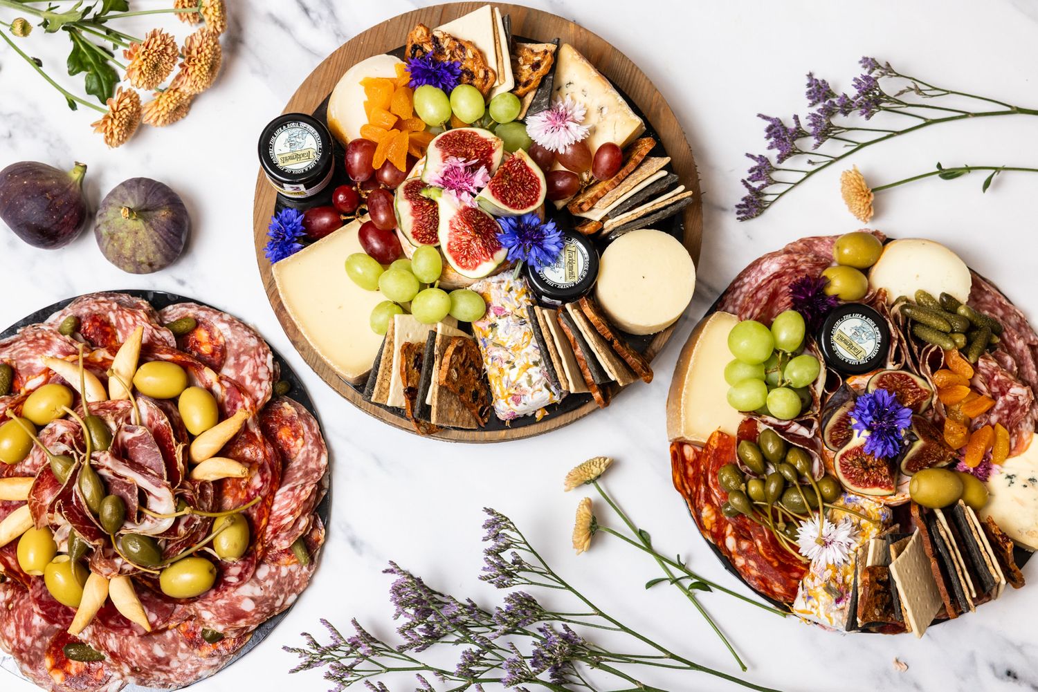 Artfully plated appetizers and dishes arranged in a row on white plates with colorful garnishes and edible flowers.