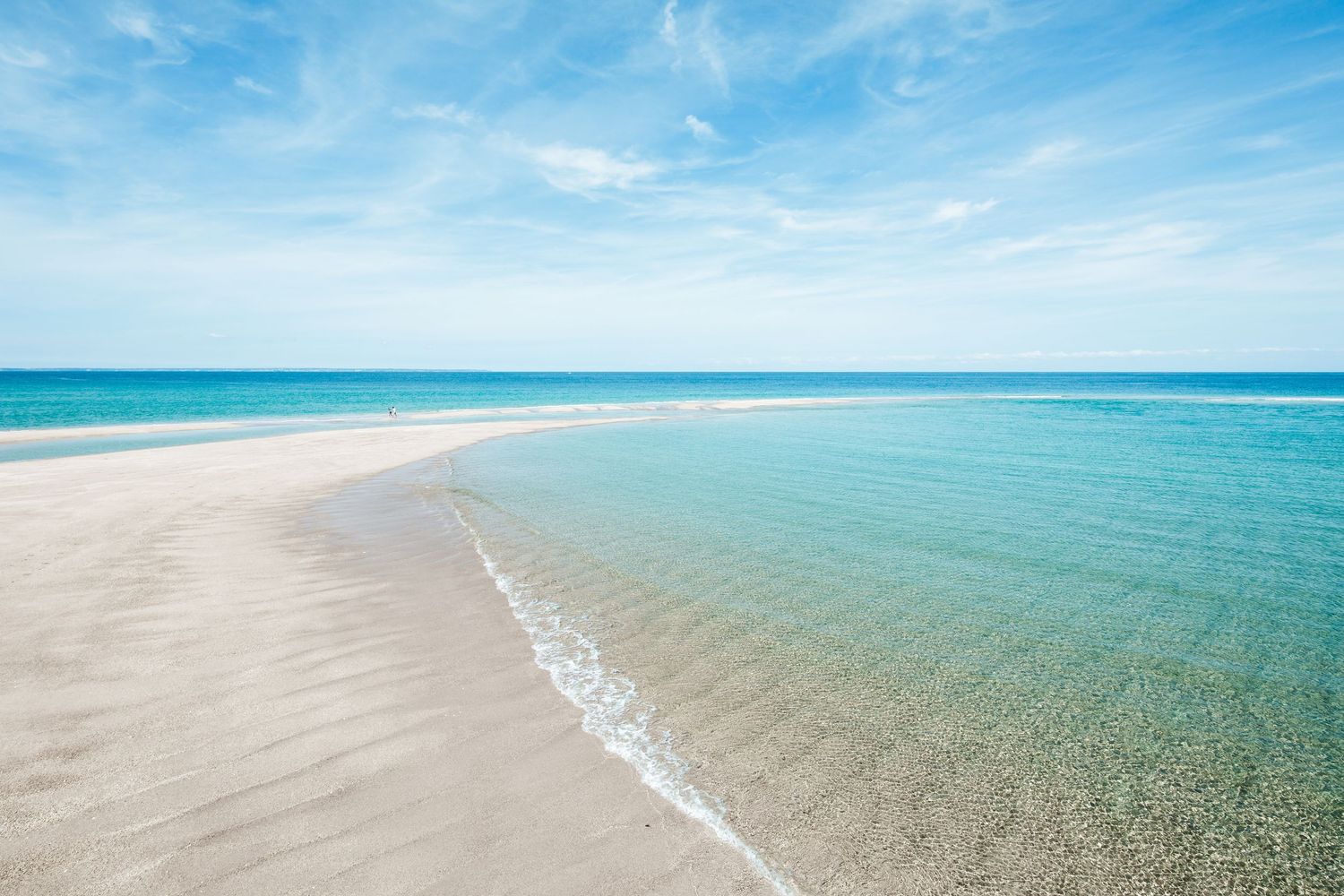 Pristine turquoise waters meeting white sandy beach under clear blue skies.