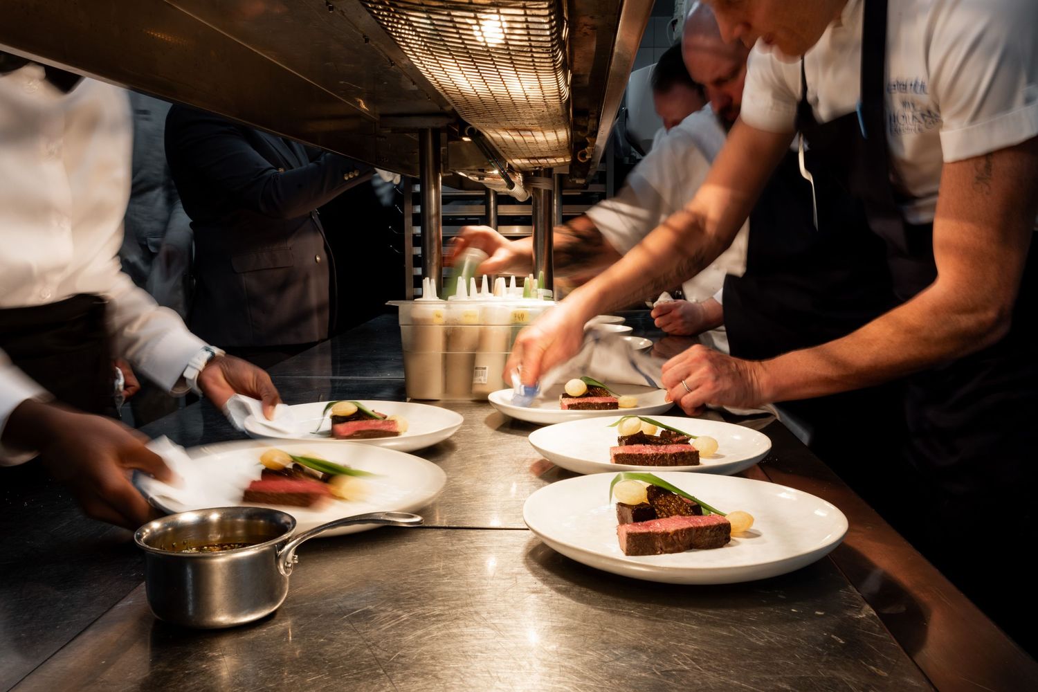 Chef adding finishing touches to plated dishes in dimly lit kitchen.
