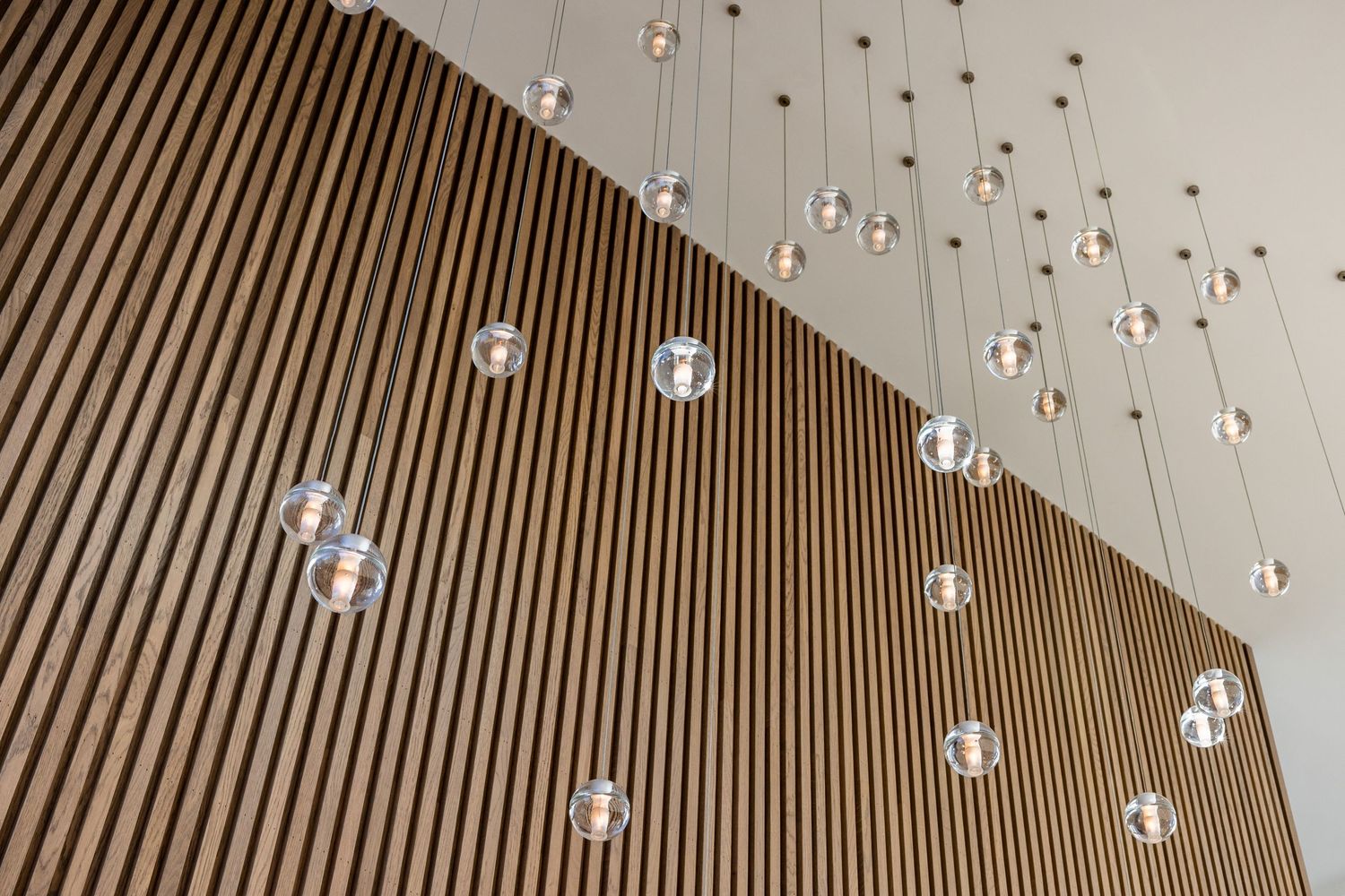 Glass pendant lights hanging from wood-paneled ceiling creating an elegant geometric pattern.