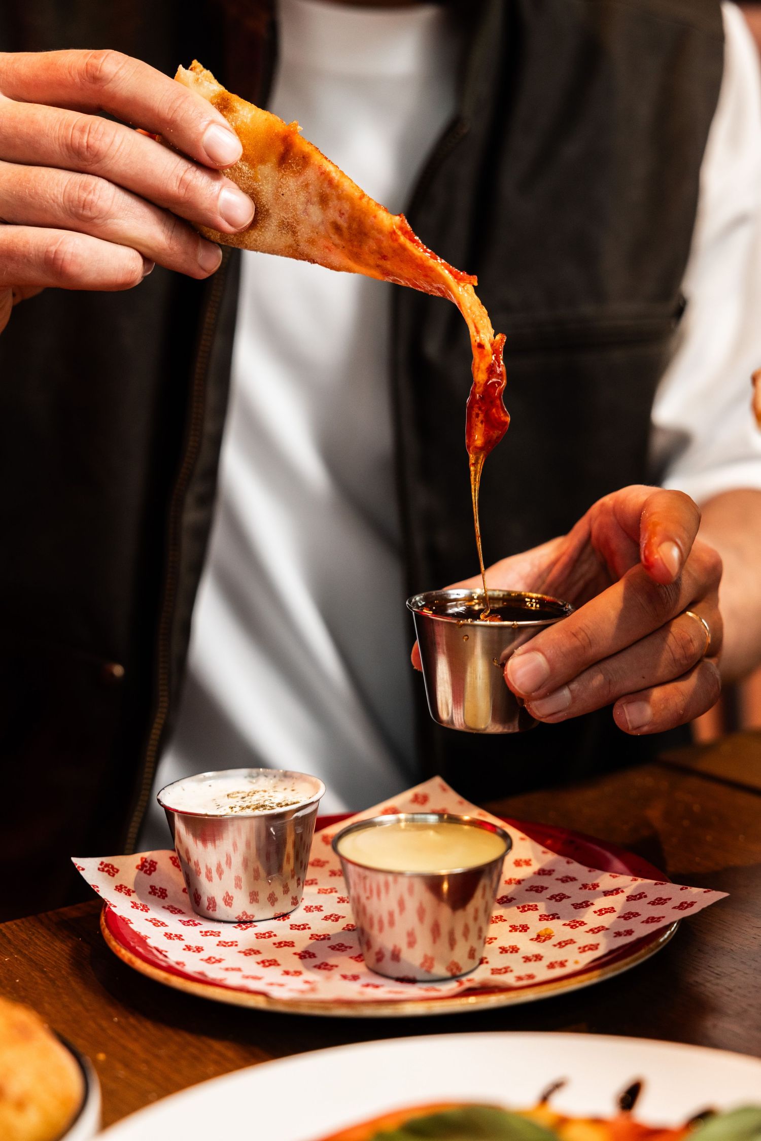 Pizza slice being dipped into sauce cups on a patterned serving tray.