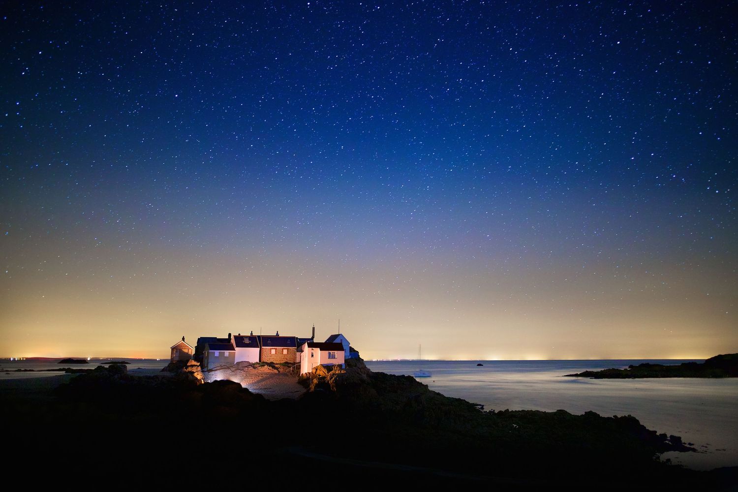 Panoramic view of a lighthouse silhouetted against a starlit night sky.