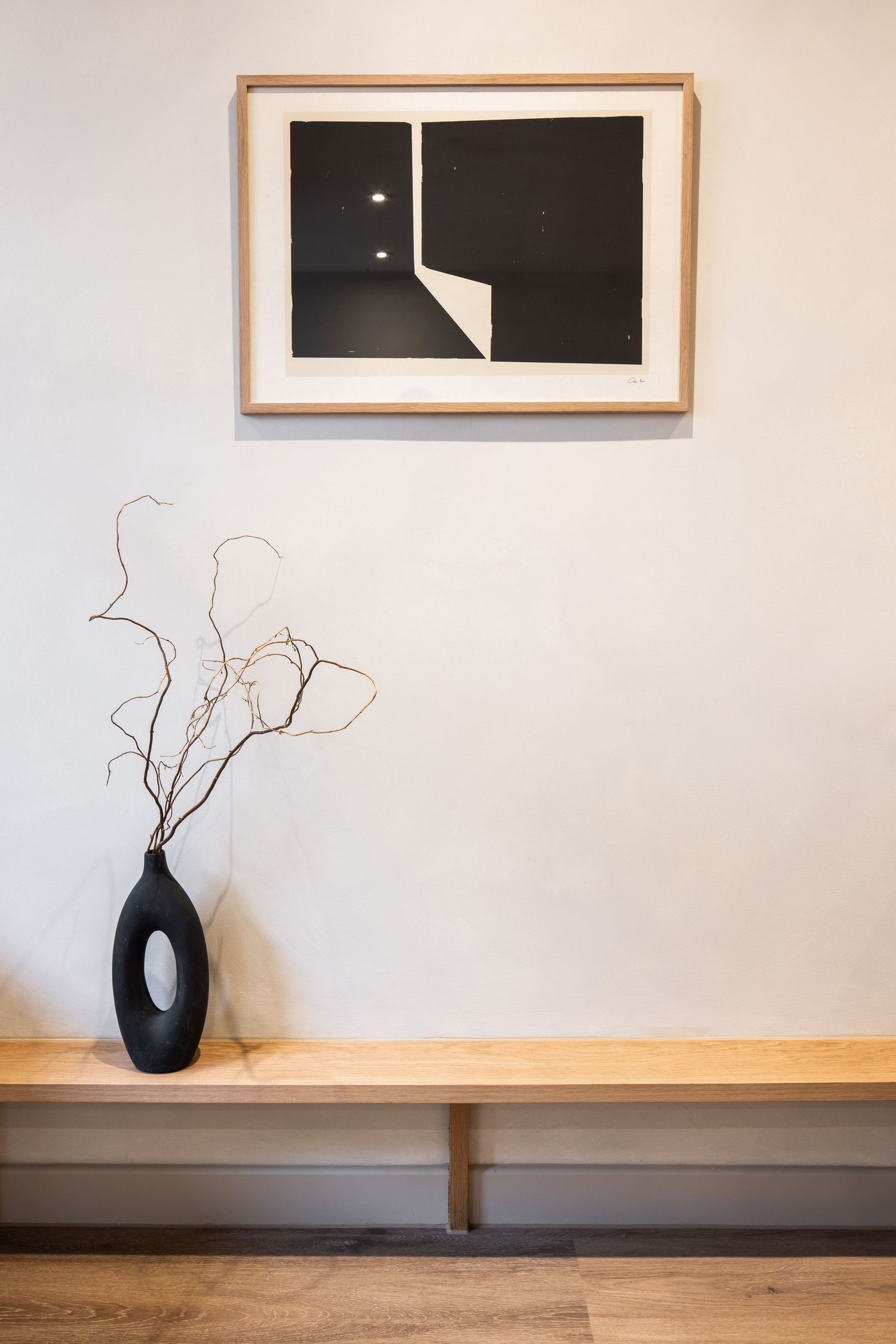 Minimalist gallery wall with black artwork and simple black vase on wooden shelf.