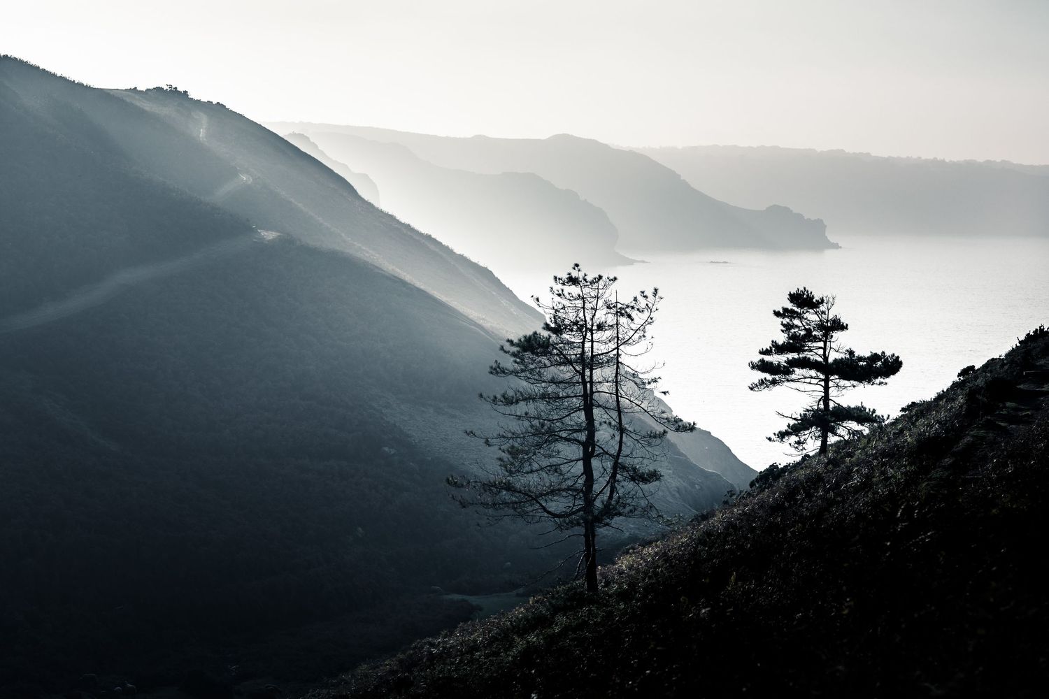 A series of misty mountain silhouettes fade into the distance creating a dramatic layered landscape effect at sunset.