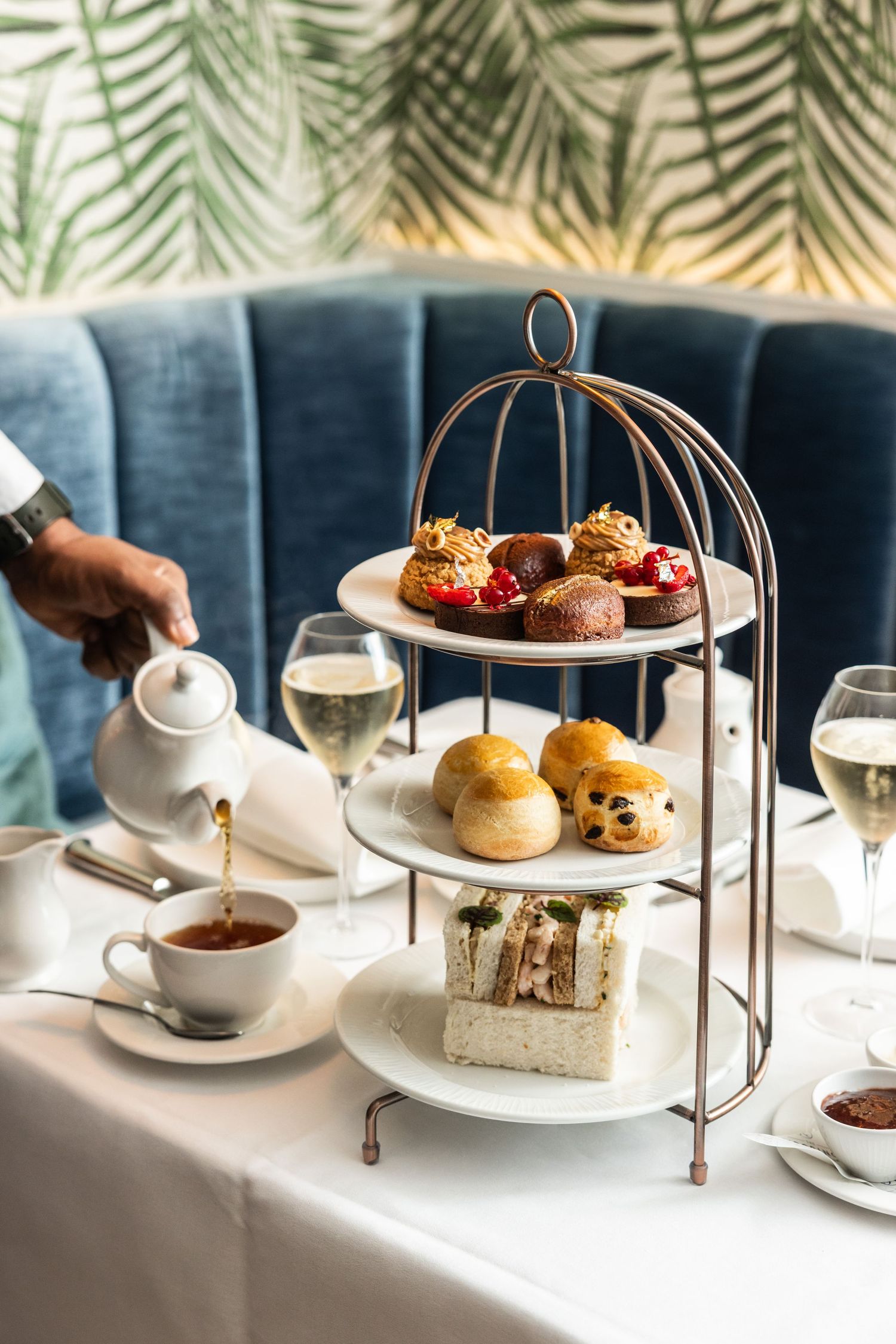Luxury afternoon tea service with tiered stand displaying pastries and sandwiches on white tablecloth.