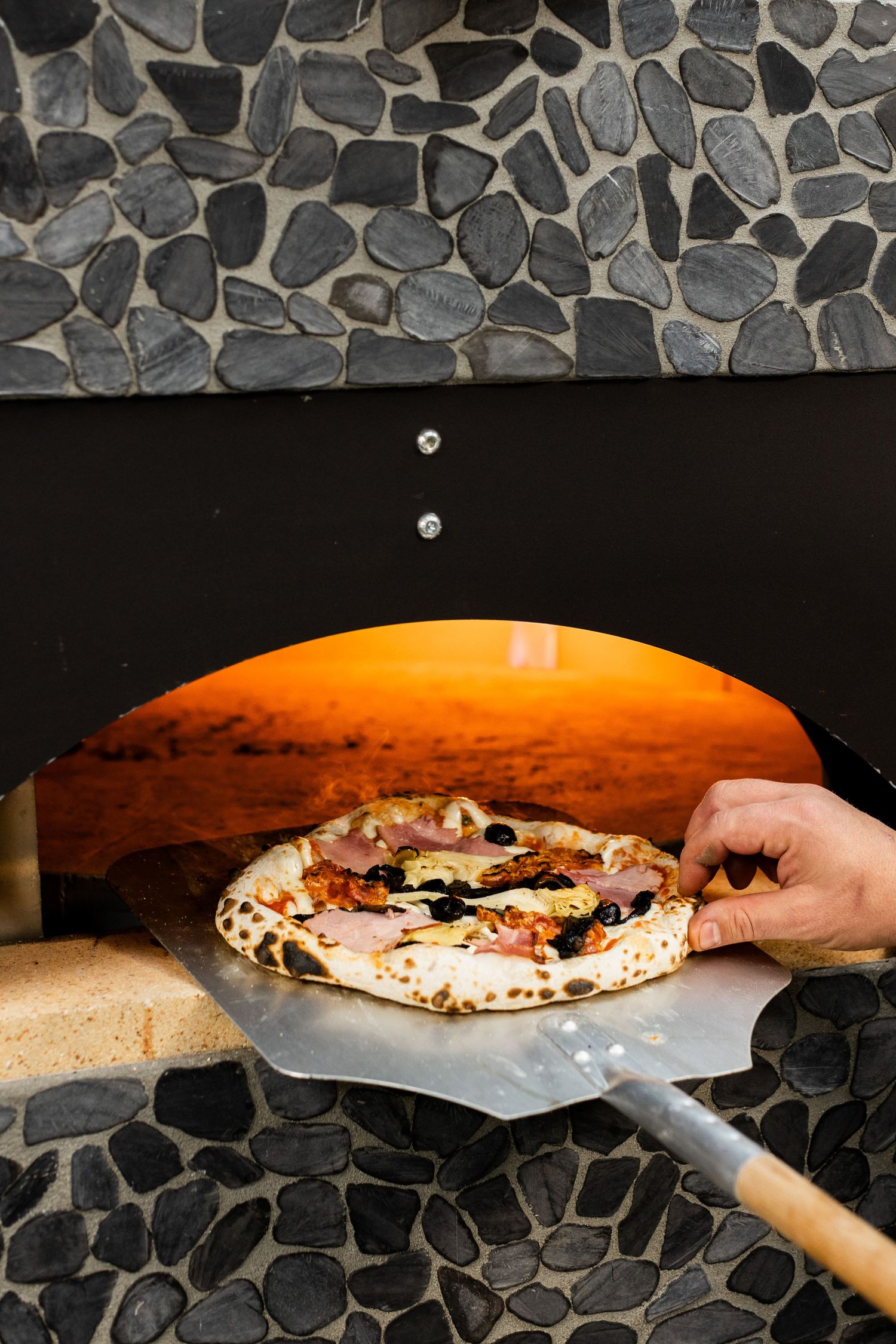 Pizza being removed from a hot stone oven using a traditional wooden pizza peel.