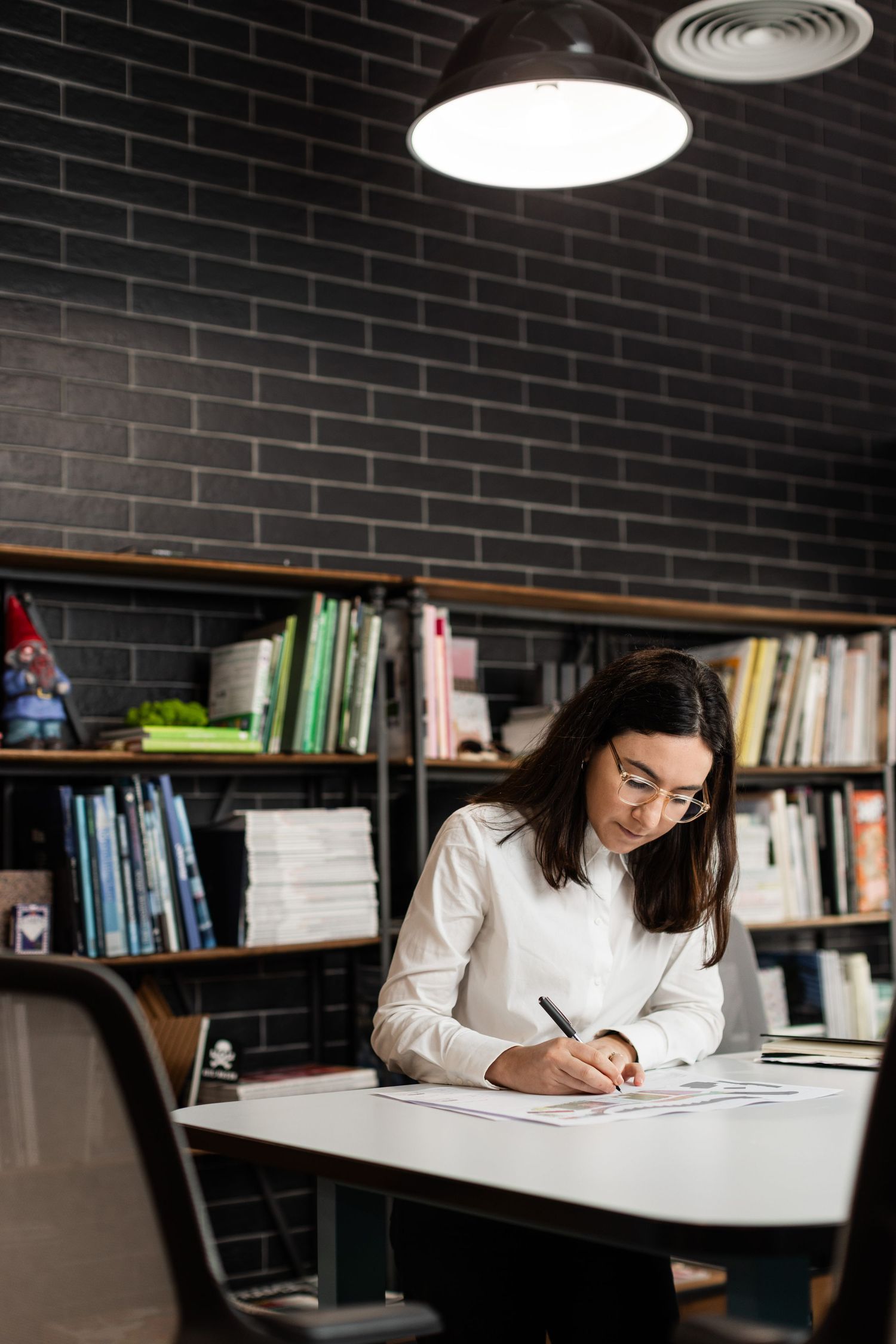 Team member at Axis Mason studying at desk in library with dark brick walls and overhead lighting.