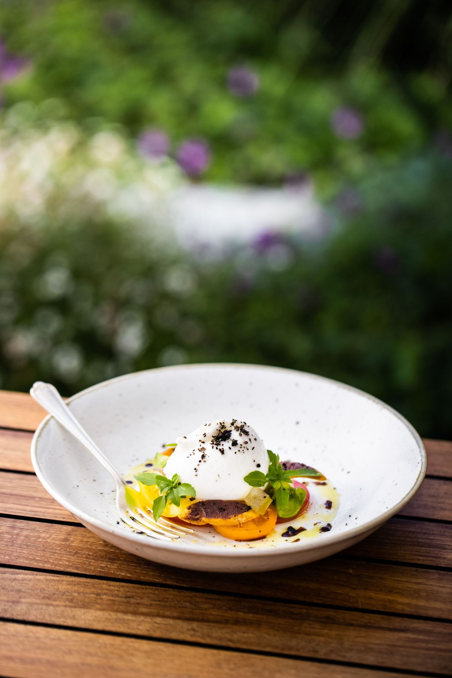 Elegant plated dish on white ceramic plate against natural garden background.