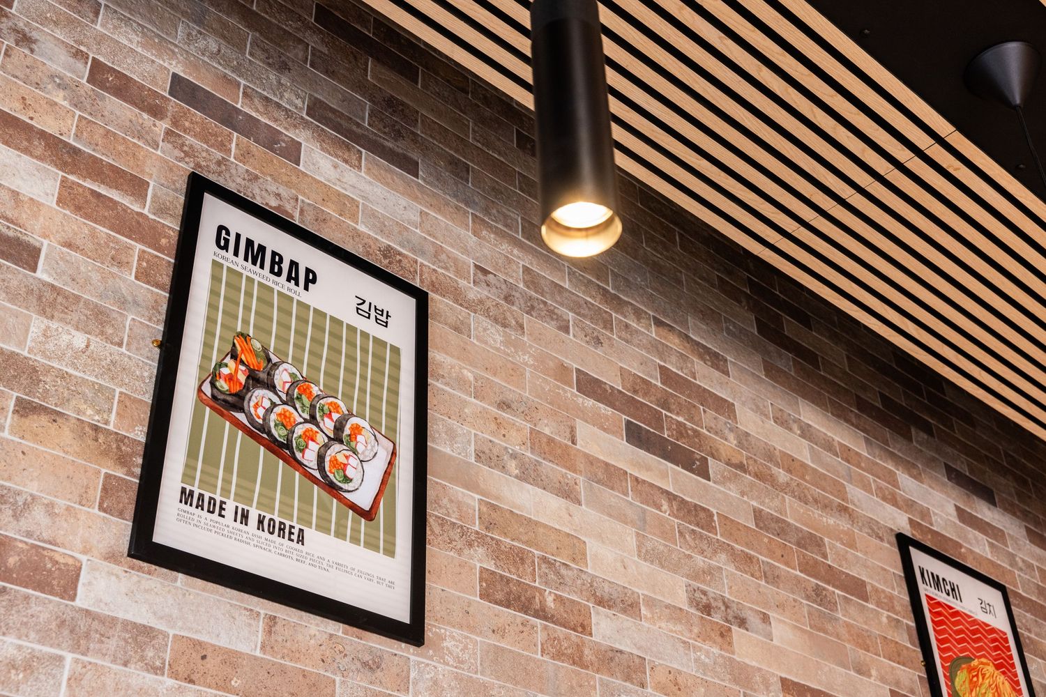 Vintage-style framed poster on exposed brick wall with wooden slat ceiling and pendant lighting.