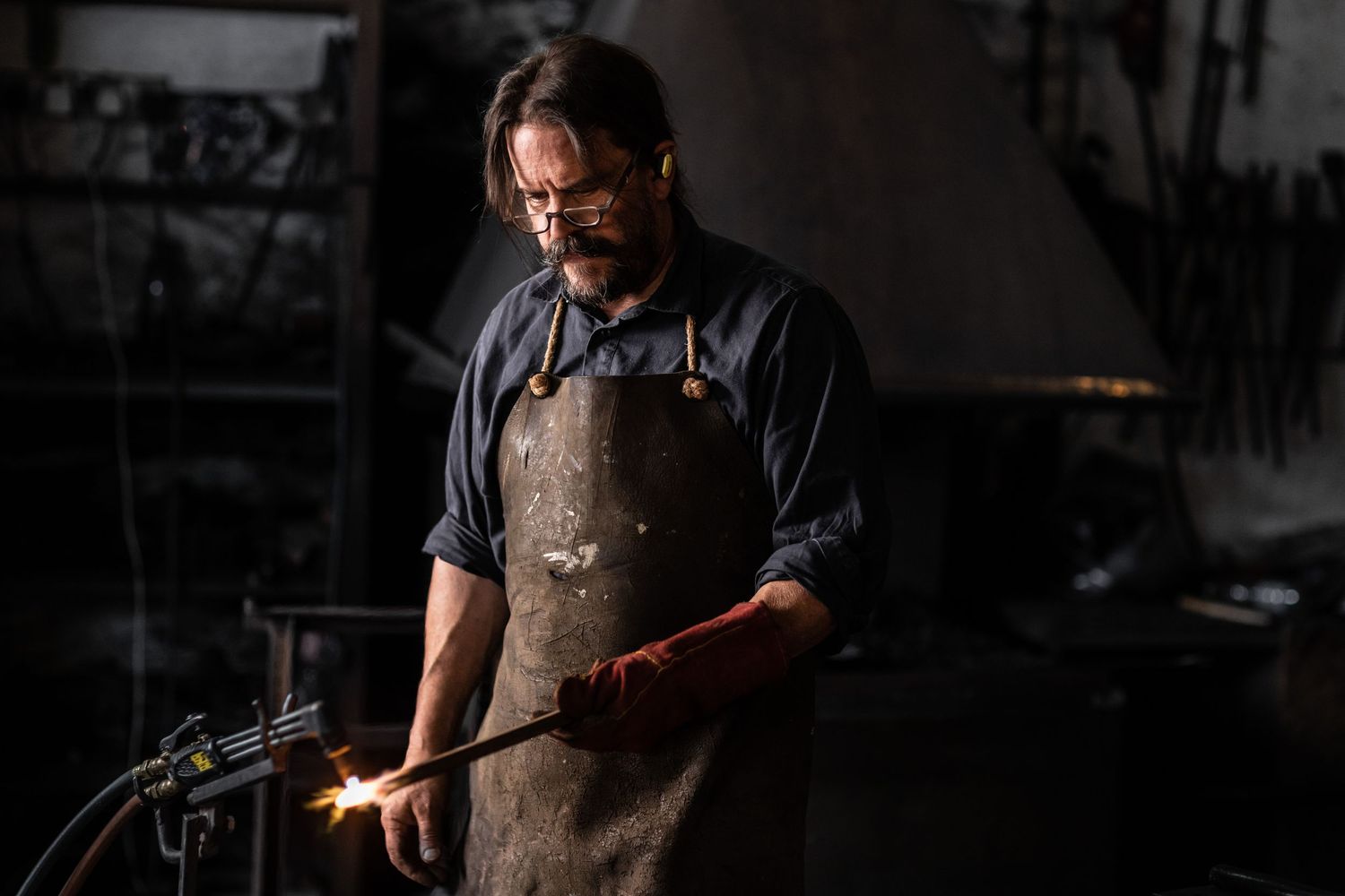 Craftsperson in leather apron working in dimly lit workshop.