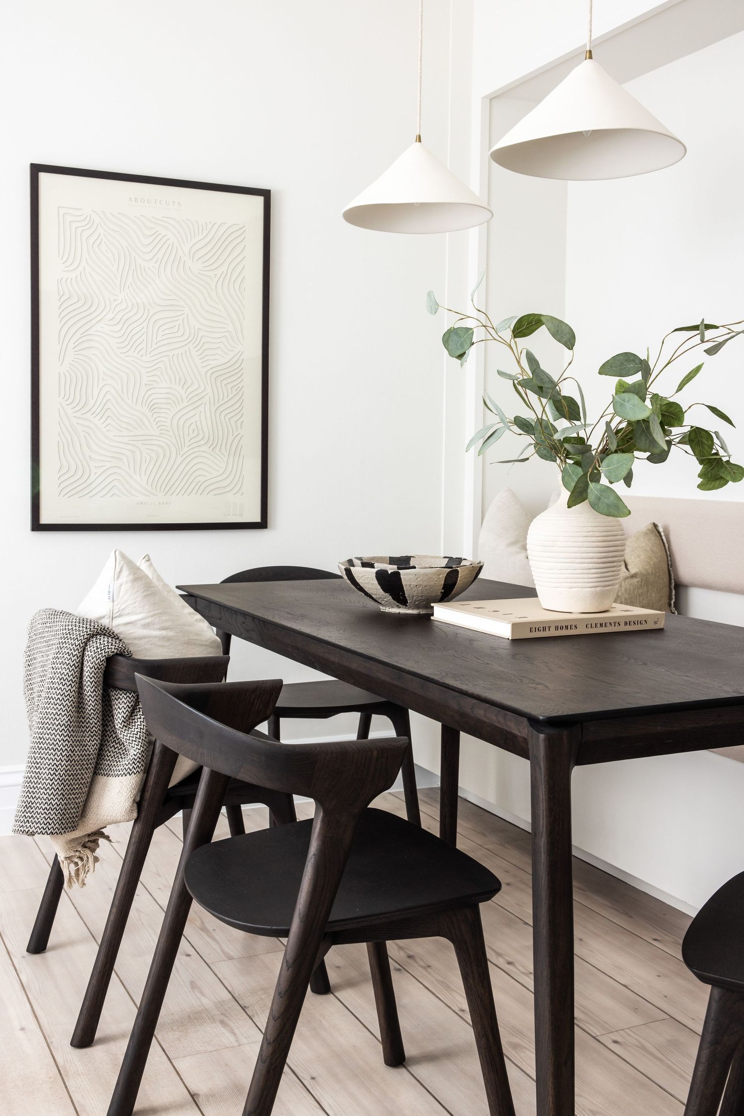Modern Scandinavian dining room with black wooden table, chairs and white pendant lights against light wood flooring.