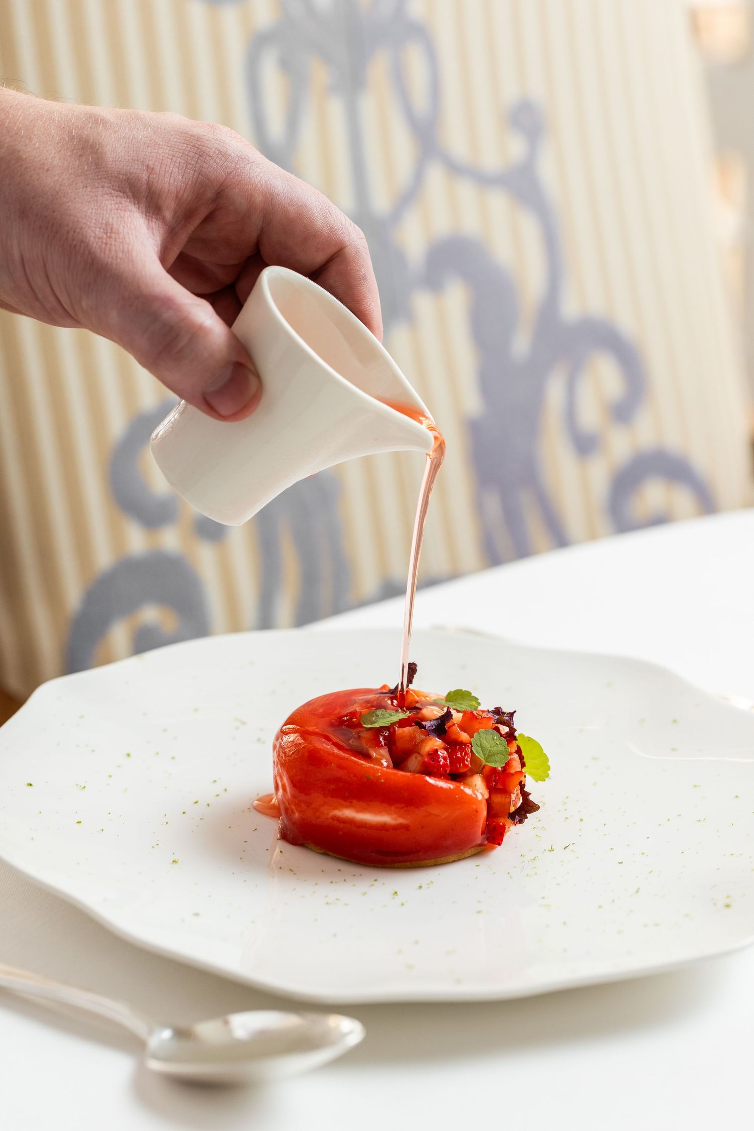 Pouring sauce over plated dessert in elegant restaurant setting.