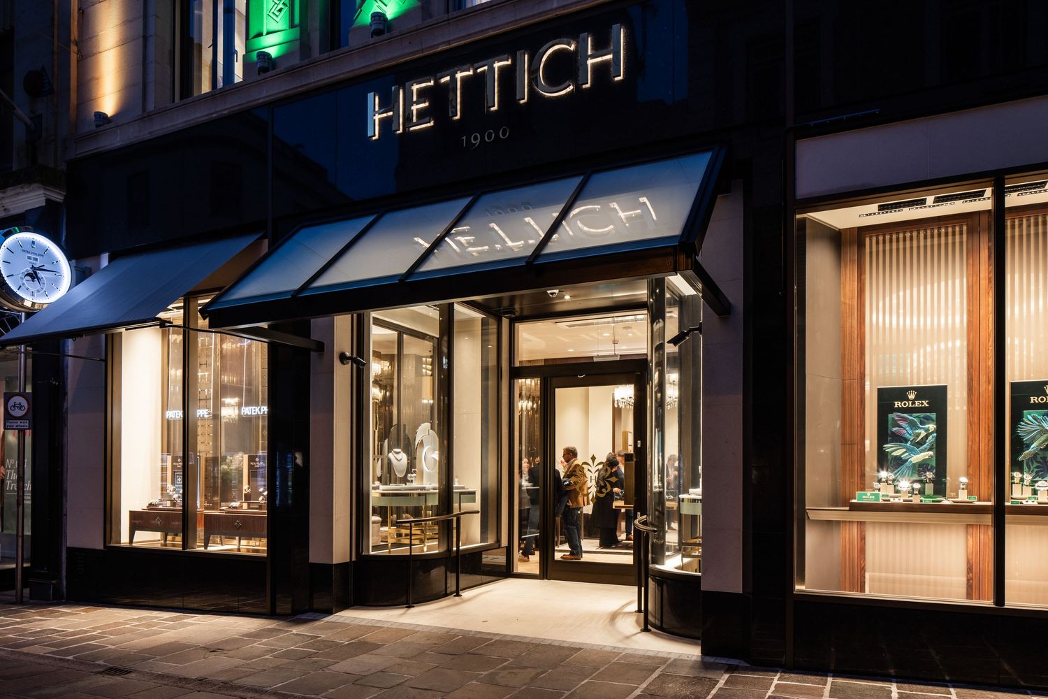 Evening view of Hettich's retail facade with warm interior lighting glowing through windows.