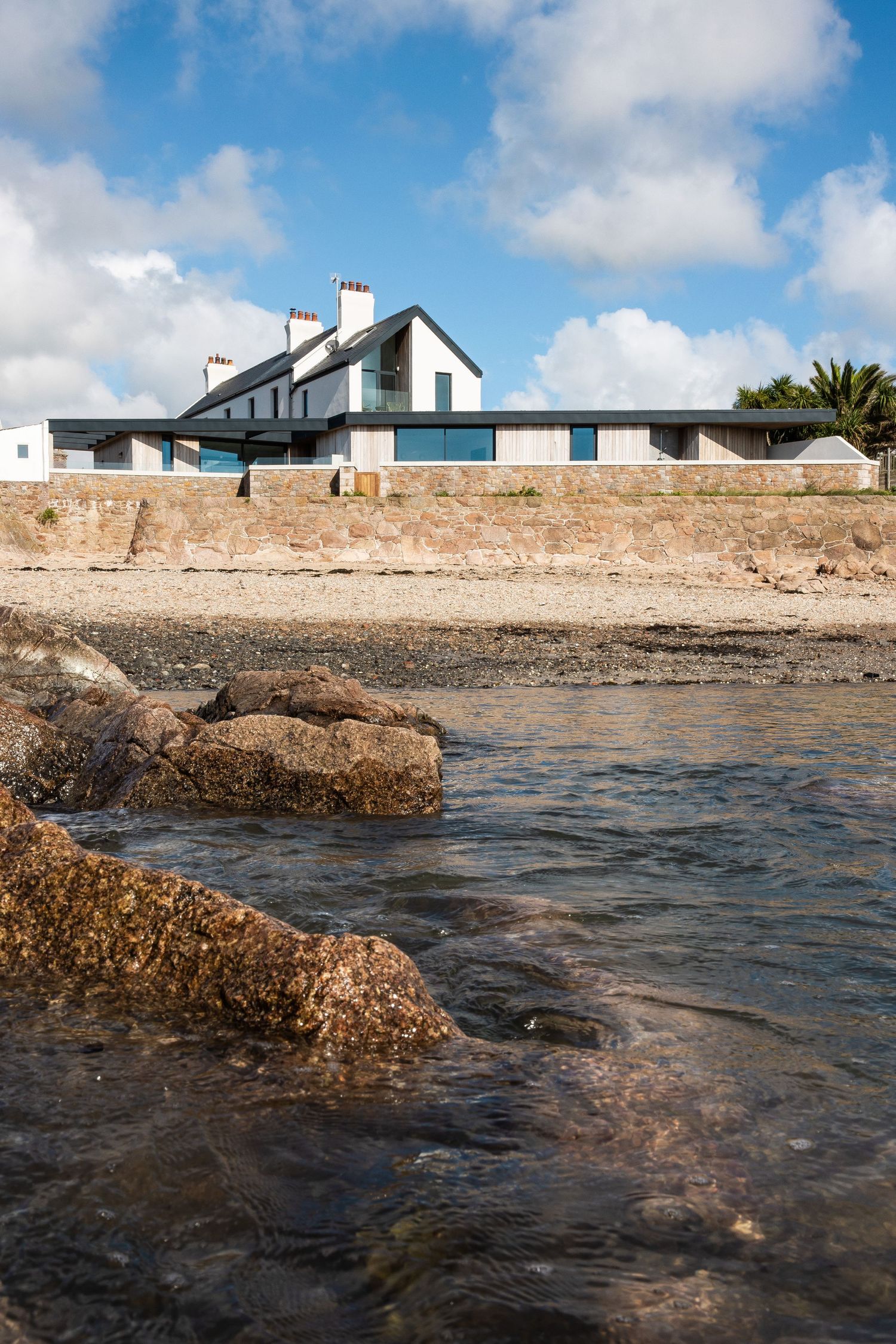 Coastal homes overlooking rocky shoreline with white buildings against blue sky.