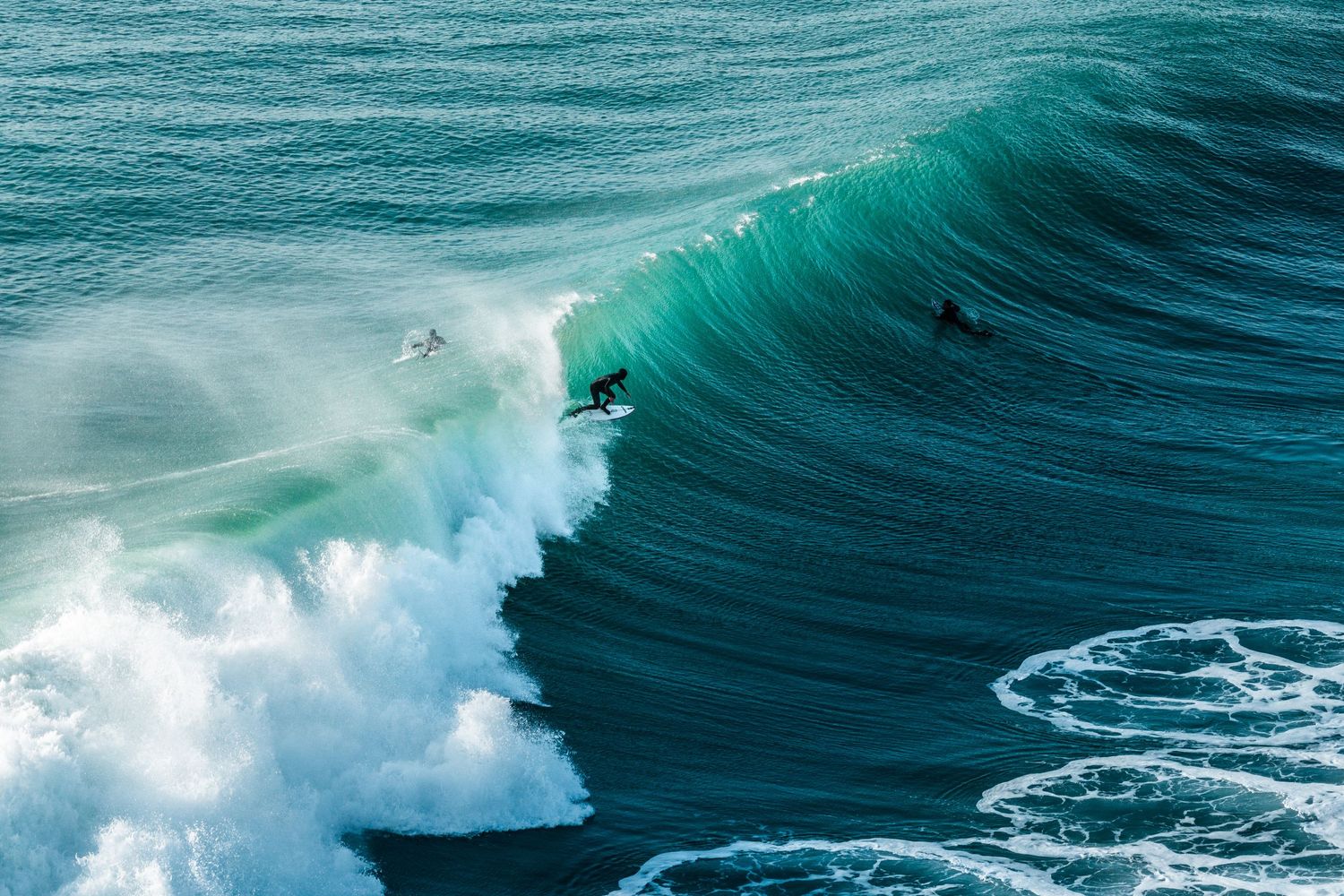 Two surfers ride a massive turquoise wave in the ocean, showcasing thrilling big wave surfing skills.