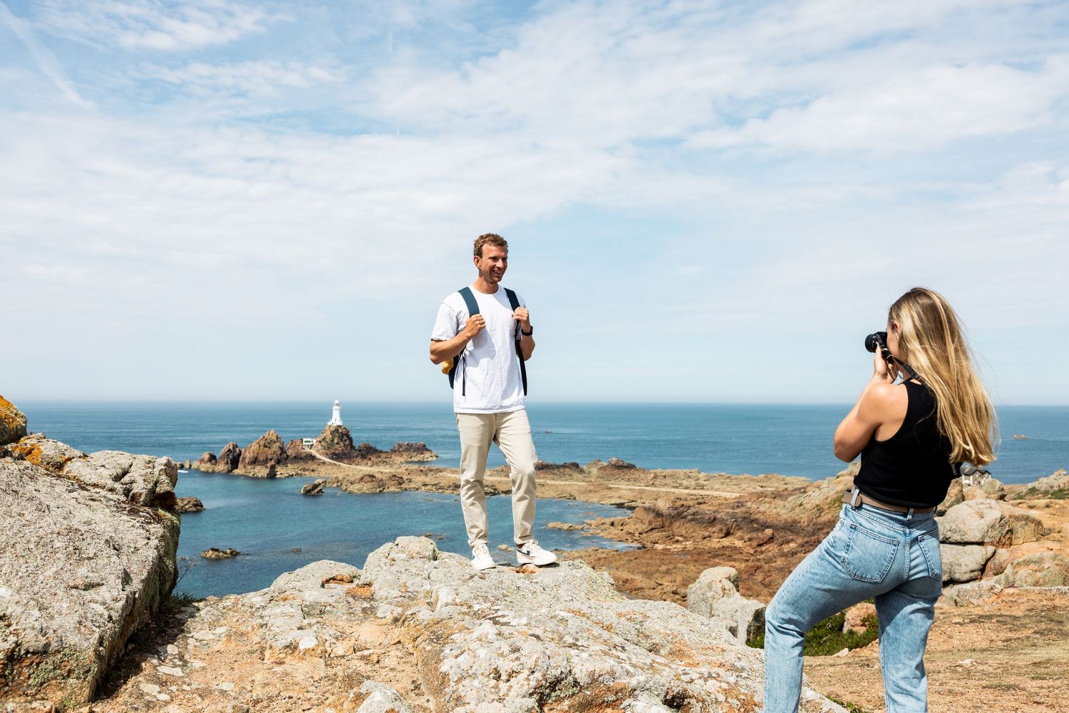 Couple taking photos on rocky coastal overlook with ocean views.