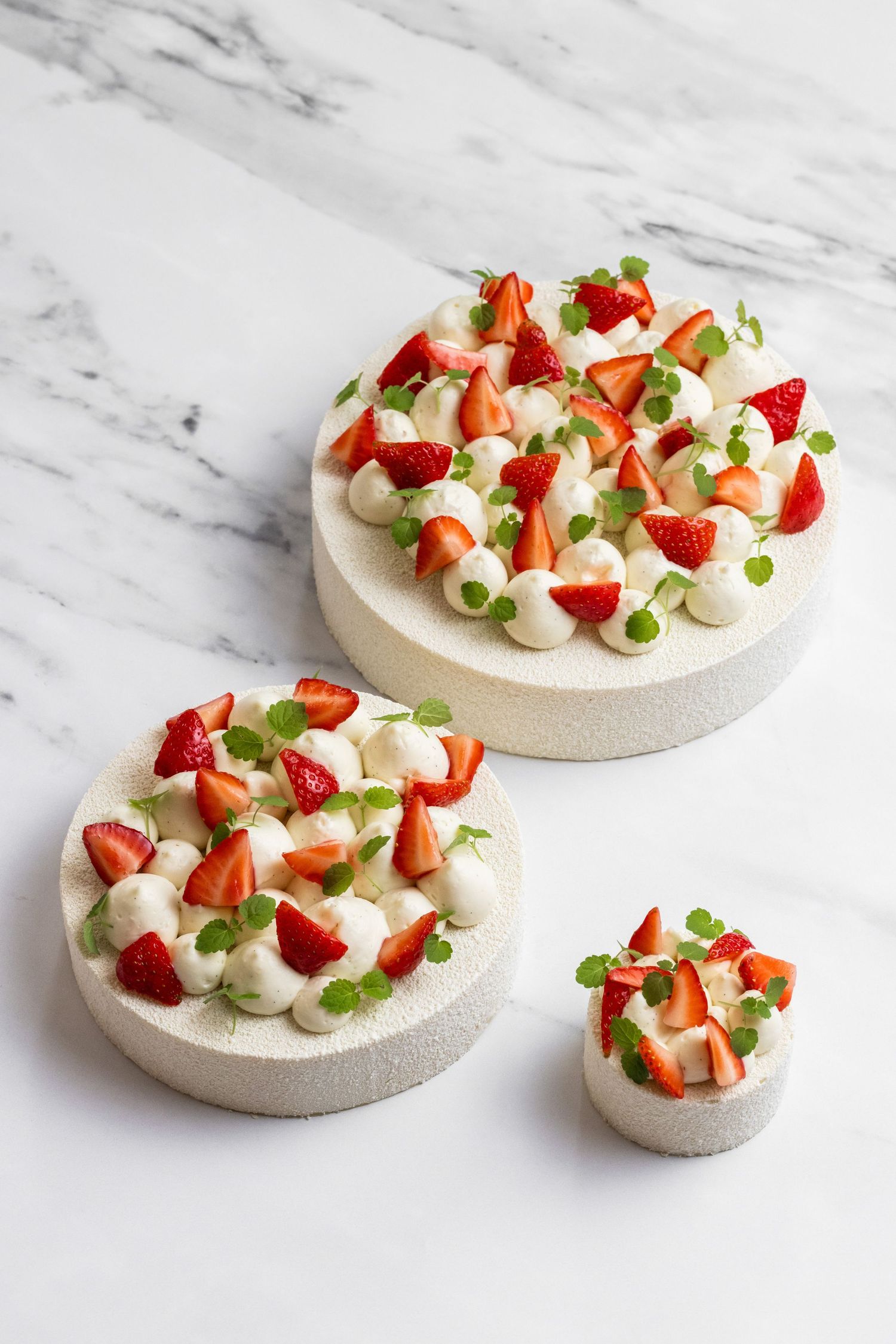 Fresh strawberry pavlova desserts decorated with cream and mint on marble surface.
