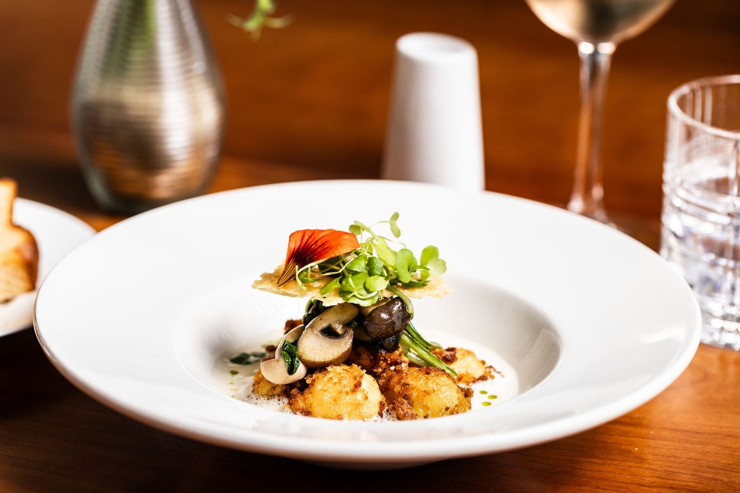 White restaurant plates with carefully plated gourmet dishes on a wooden table.