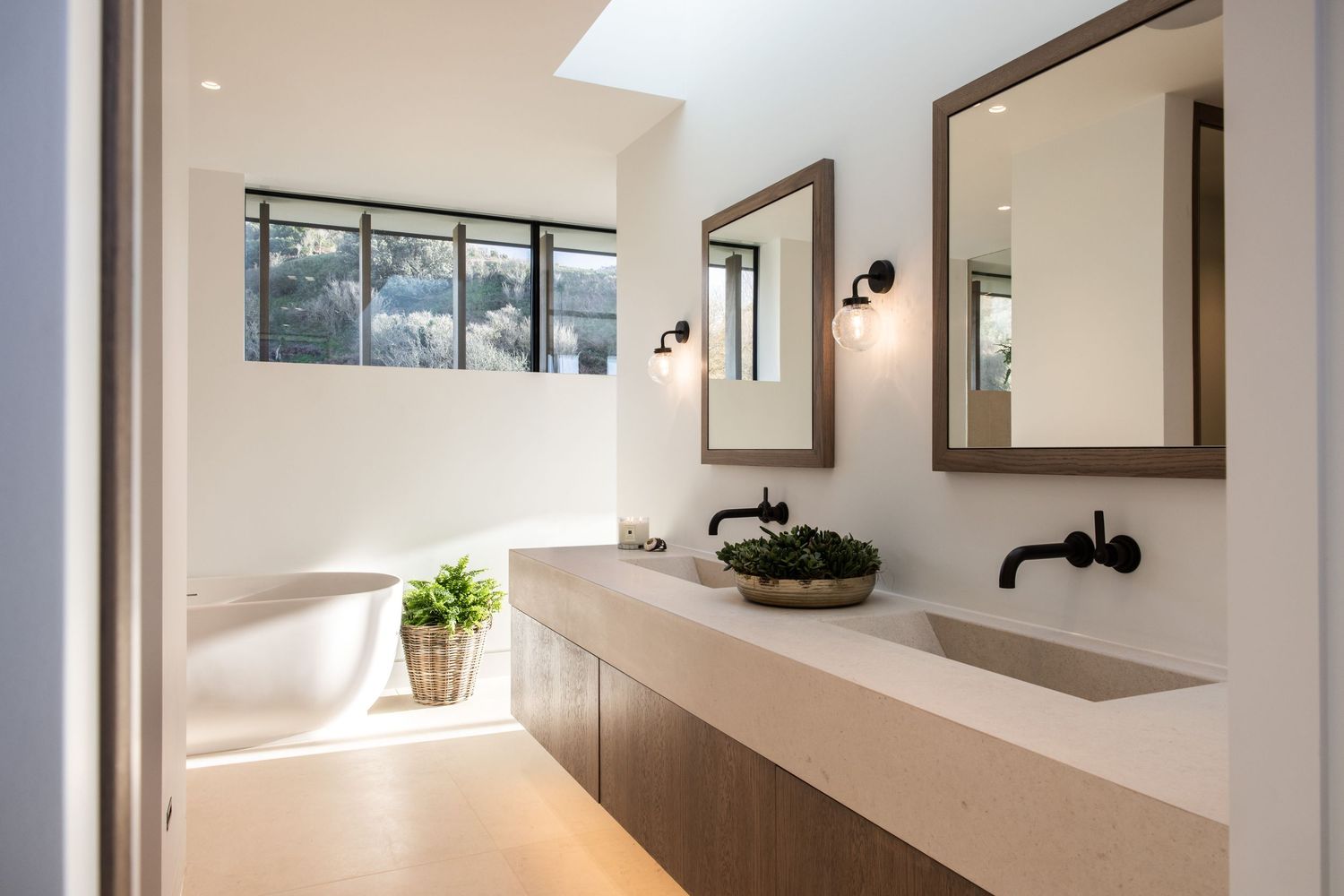 Minimalist bathroom with floating vanity, black fixtures, and natural light from skylight.
