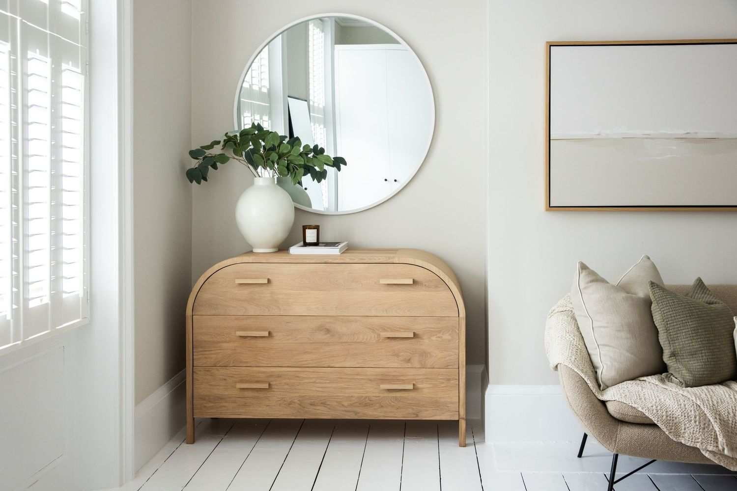 Serene bedroom interior with round mirror, wooden bed frame and white linens.