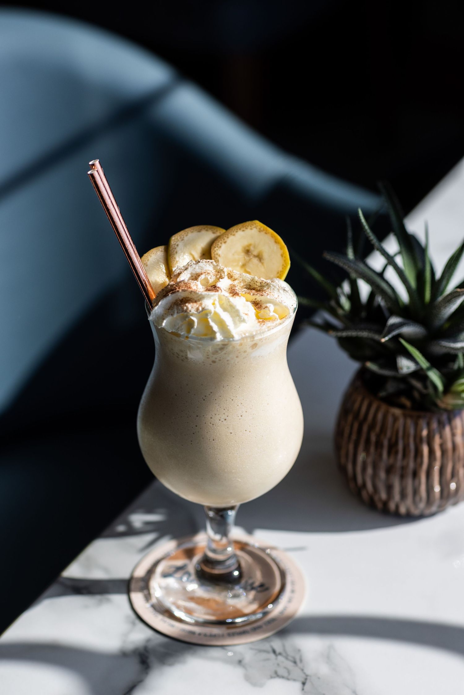 Creamy dessert cocktail garnished with banana slices and straws in a stemmed glass.