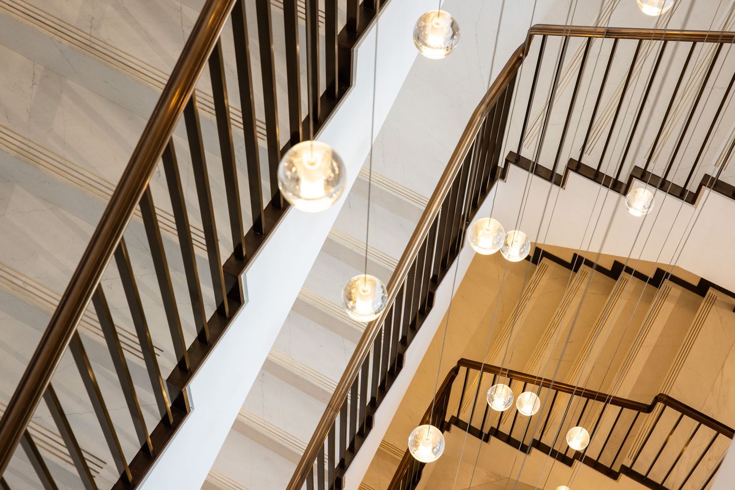 Modern stairwell featuring pendant lights and dark wood railings against white walls.